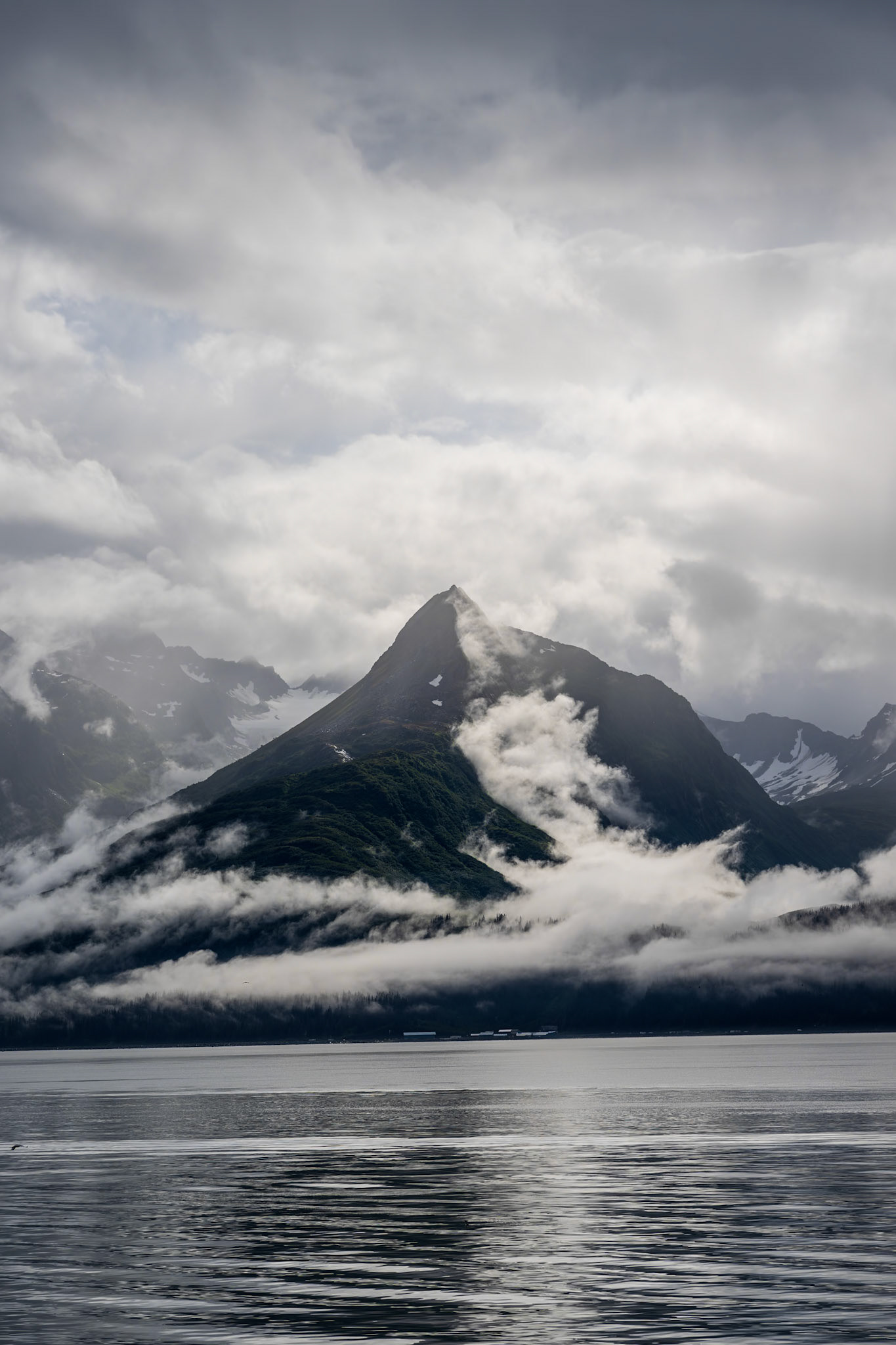 A mountain peak emerges from the clouds and mist above the Port of Valdez.