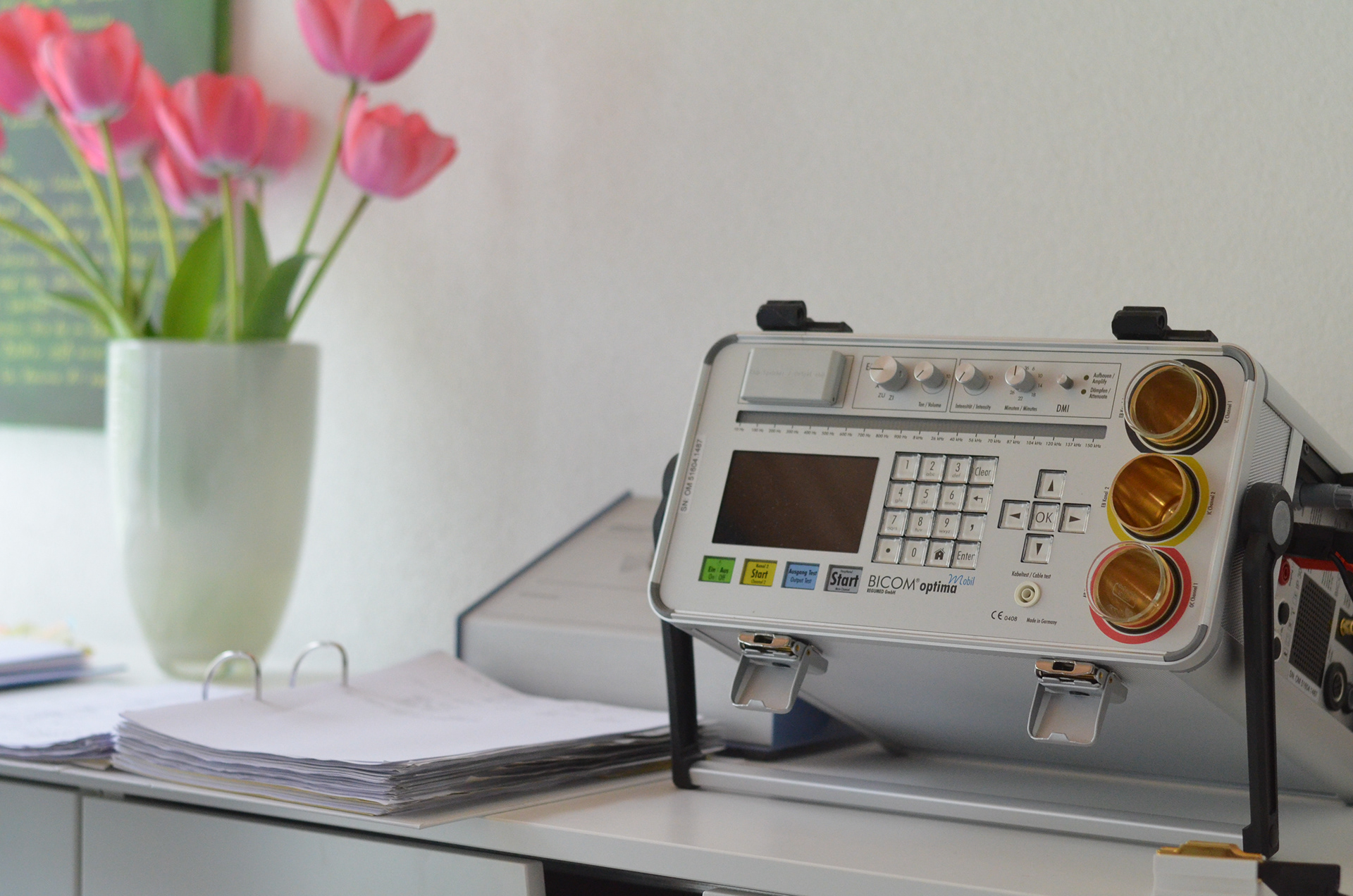 Blick auf einen Arbeitsplatz mit Bioresonanzgerät und einem Strauß Tulpen.