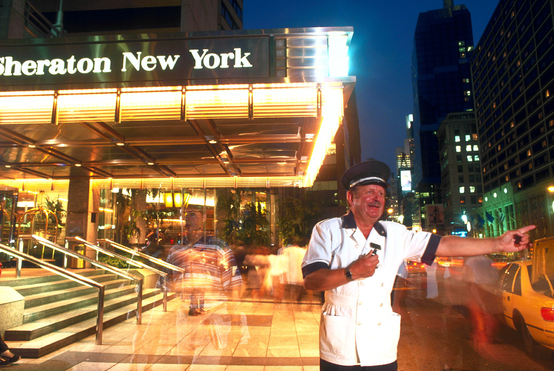 Doorman John Asuelis hails a cab in front of the Sheraton New York Hotel on Broadway in times Square.  Photographed for Fortune Magazine.