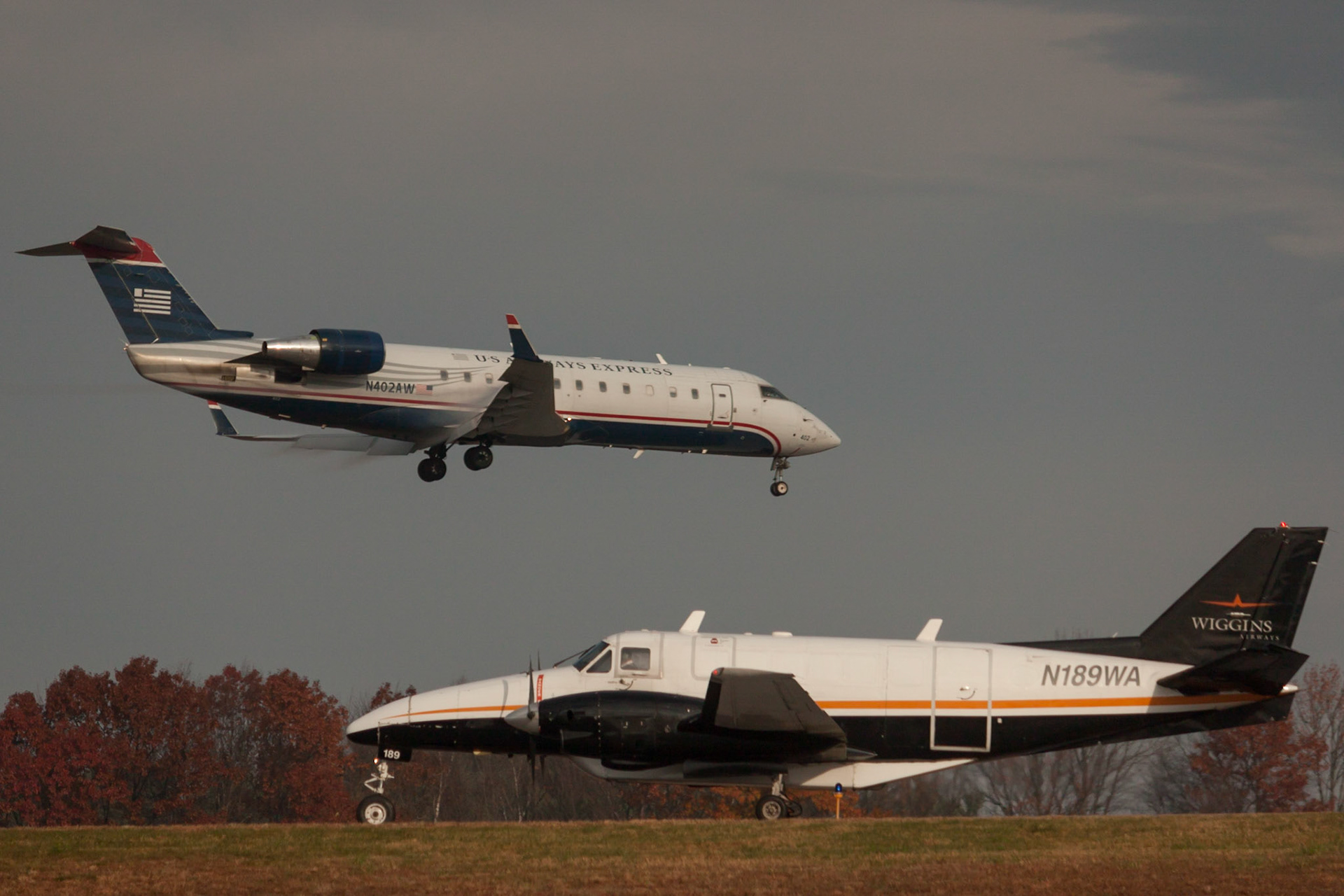 Beech 99 (N189WA) of Wiggins Airways waits while Bombardier CRJ200 (N402AW) of US Airways / Air Wisconsin lands in Manchester in November 2015.
