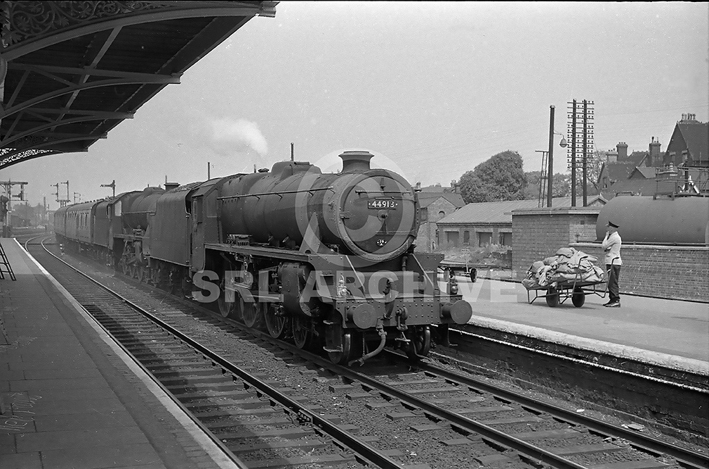 44918+45712 double head on an Up express through Bedford (Midland Road) station in June 1960. A postal worker waits with his trolly full of mail bags for the morning delivery. SRL No 1159 