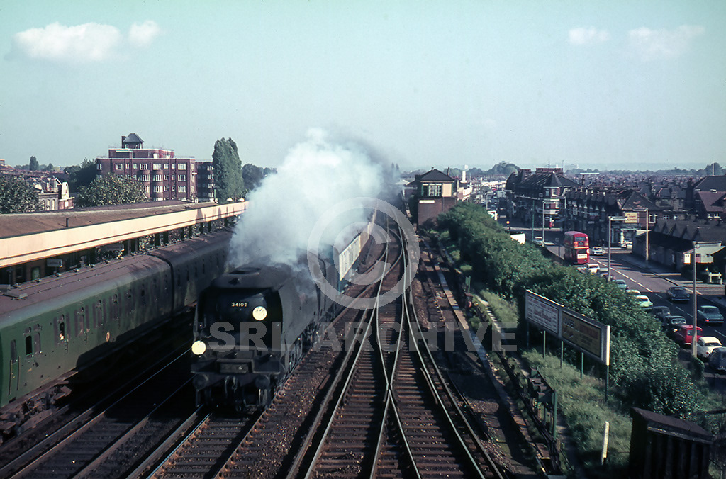 34102 'Lapford' going well through Raynes park station with a Waterloo-Bournemouth express 21st October 1966. On the right we see a busy high street with some period vehicles of the day. SRL No 1170