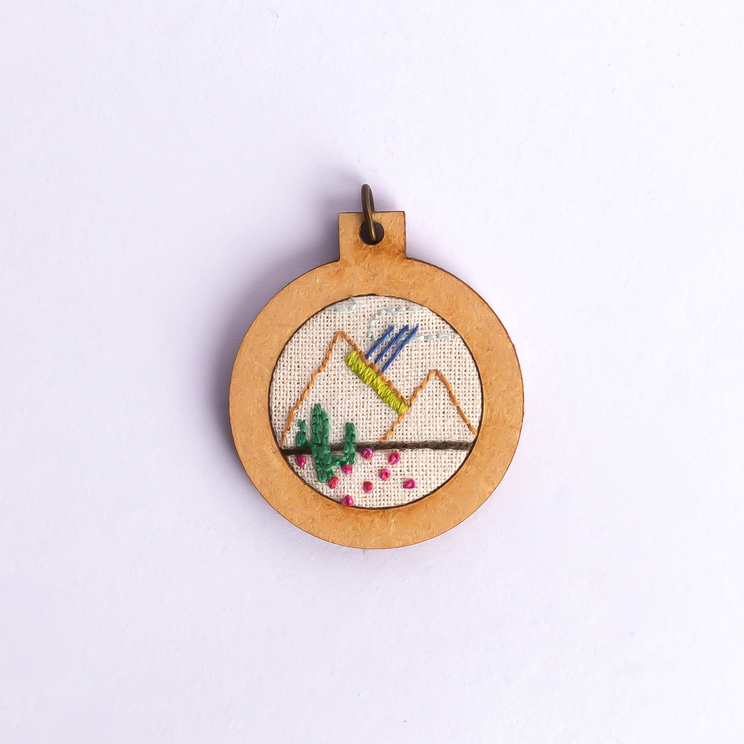 Dije bordado a mano con marco de madera y cordón de hilo encerado. Pieza única. Tamaño 3cm de diámetro. $10.000