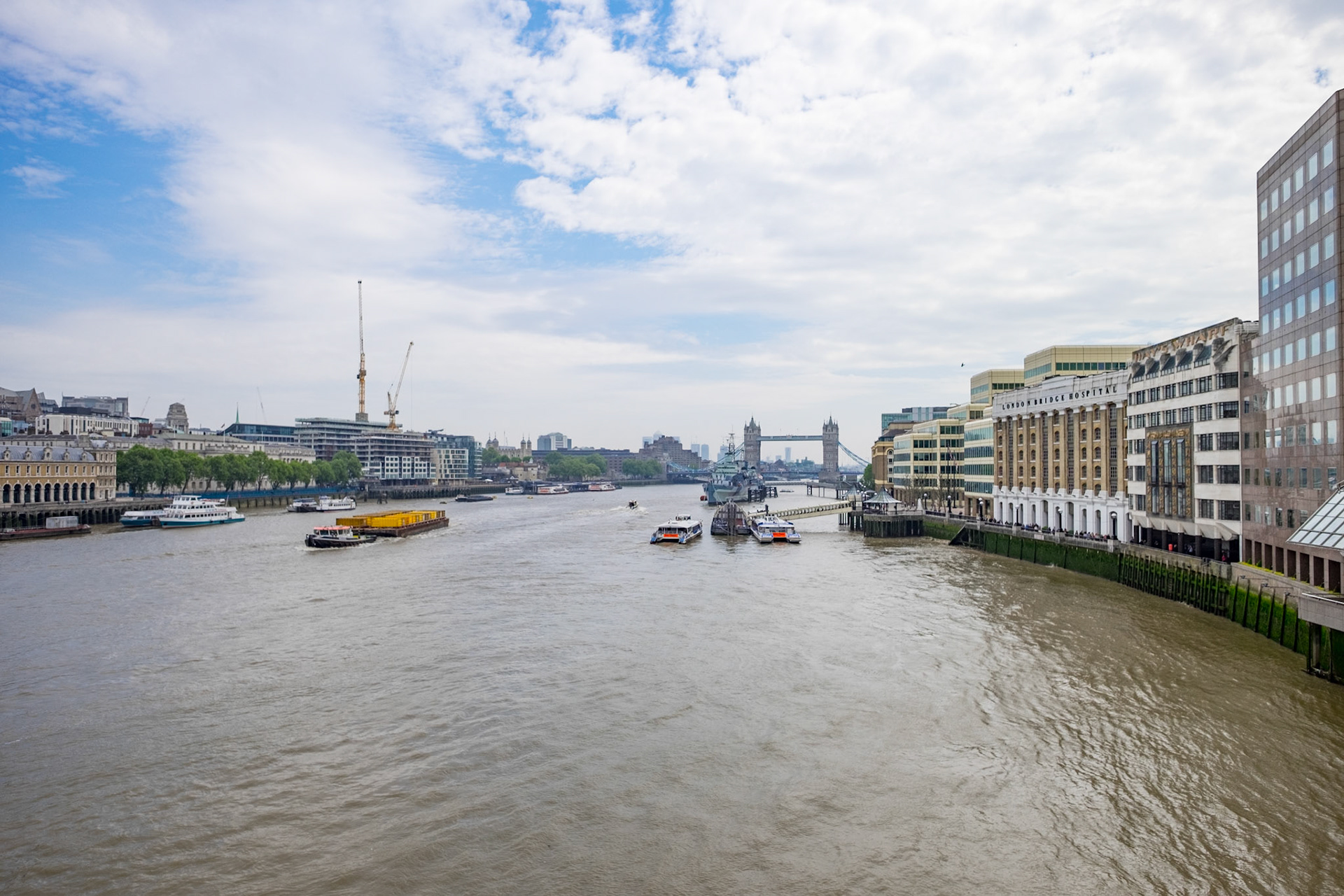 London's great tower bridge seen from the south side of the london bridge. Ships passing by under a cloudy sunny sky.