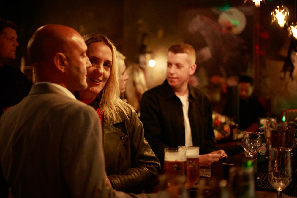 Guests chatting at the bar, one glancing at the camera