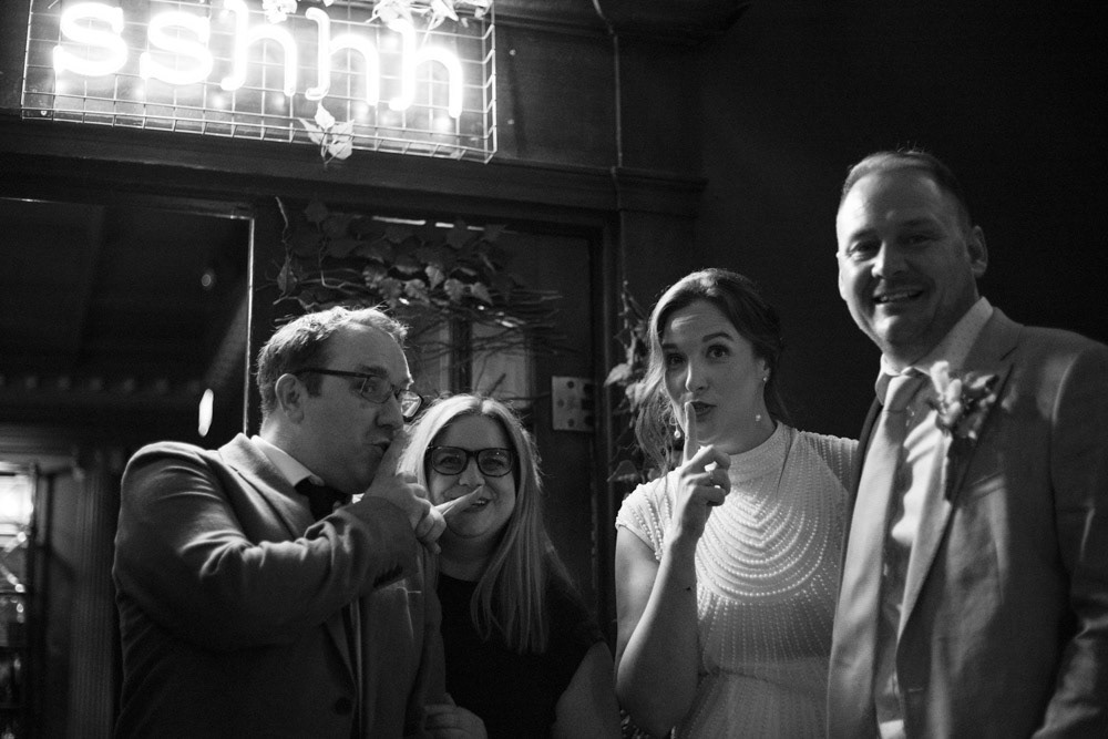 Couple and best man posing with a neon “shhh” sign at Lost & Found Leeds Club