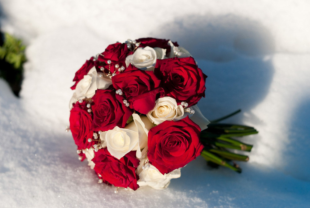 Red and white bridal bouquet photographed in February snow and sunlight
