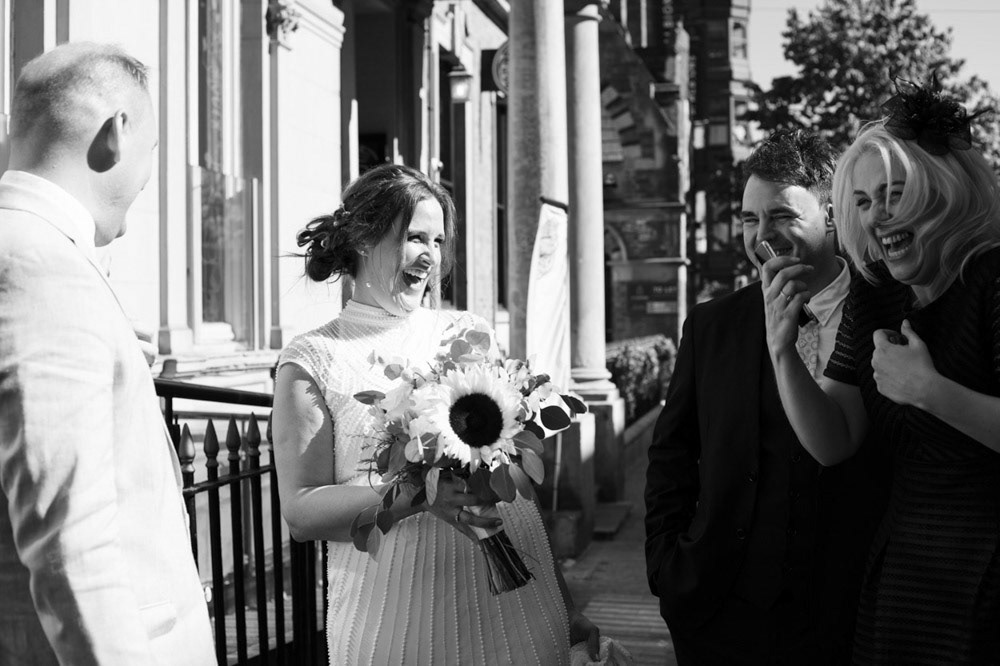 Bride laughing with family in black and white outside Leeds venue