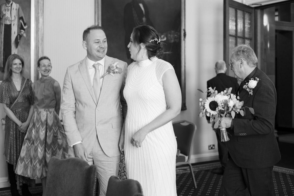 Bride arrives at Civic Hall, handing bouquet to father, friends beaming around her