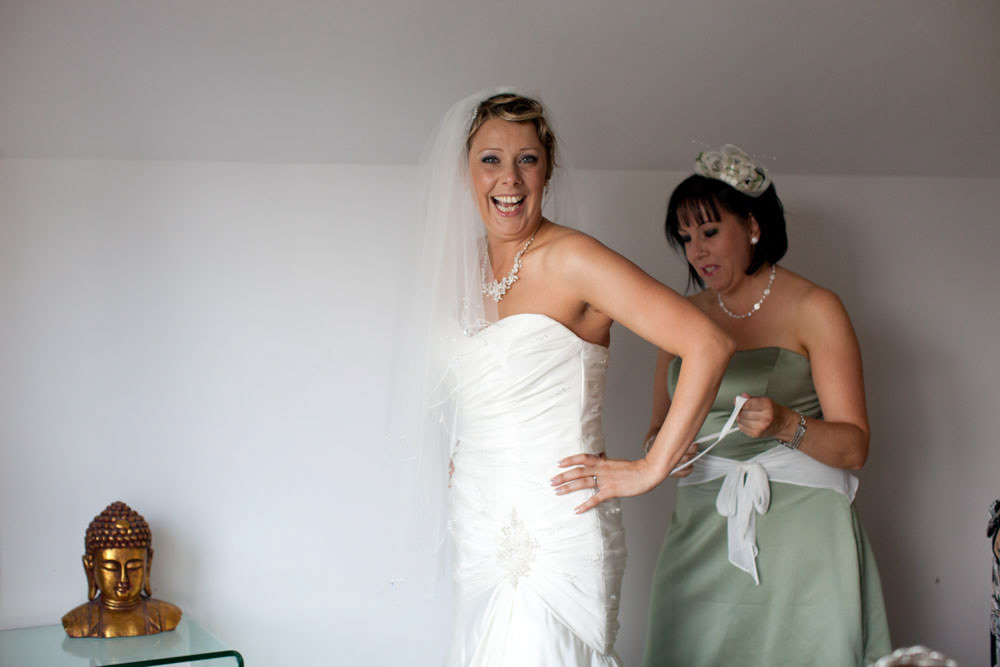Smiling bride as her bridesmaid helps fasten her wedding dress.