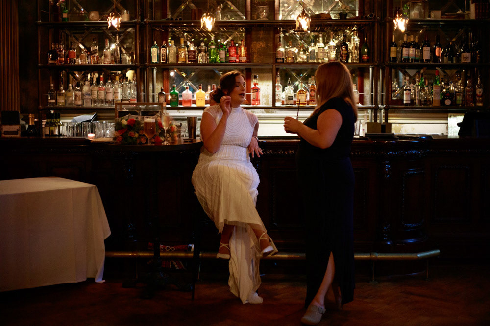 Bride Gemma talking to a friend at the bar in golden evening light