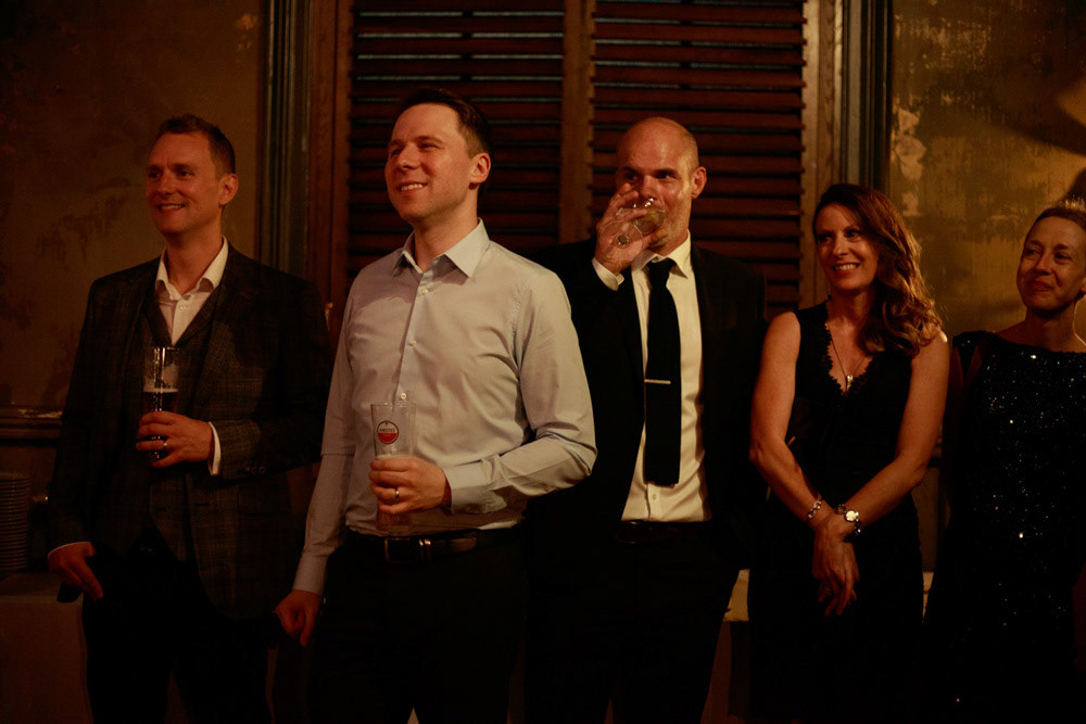 Wedding guests react with smiles to the groom’s words