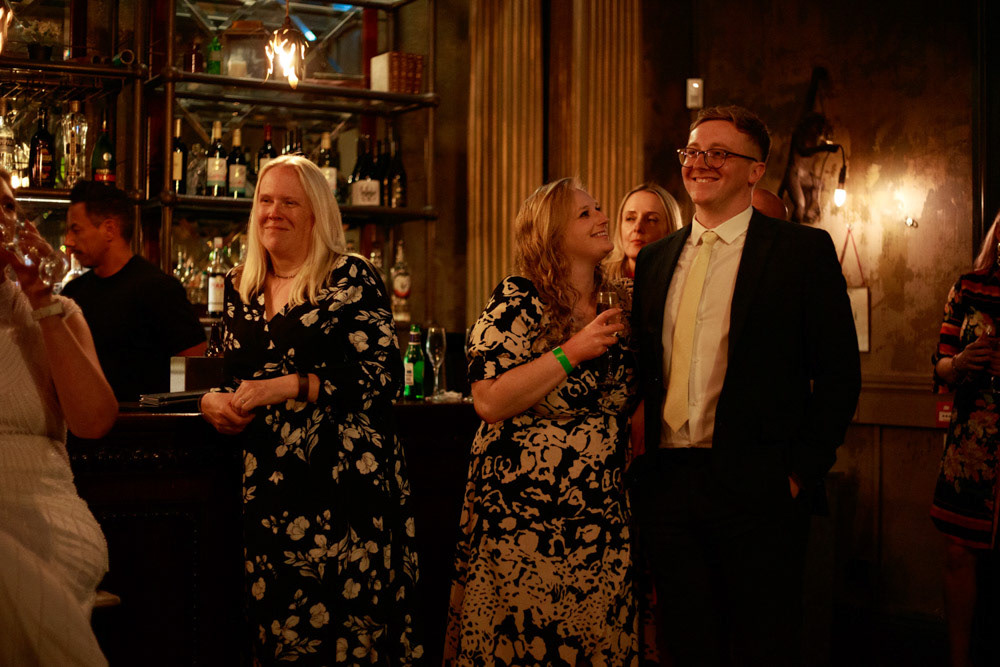 Standing guests smiling as they listen to the speech