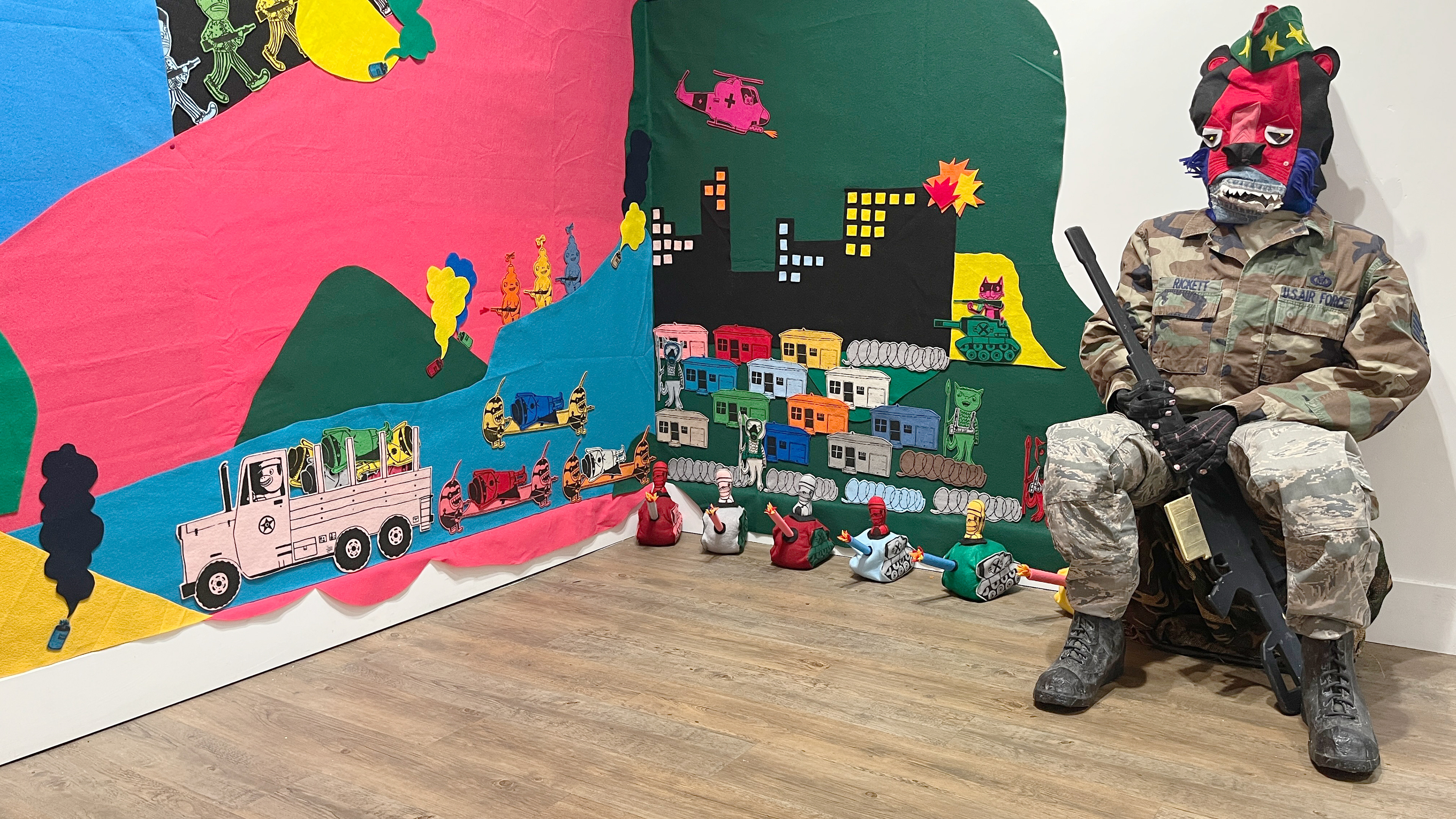 "WAR is FUN!" Screen Print on Felt, Hand cut, Hand sewn mini-tanks and Hand sewn head and hands on soldier. Cast papier-mache boots with latex