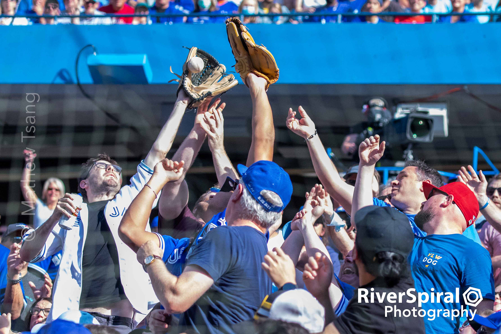 A fan snags a foul ball while holding his beer.