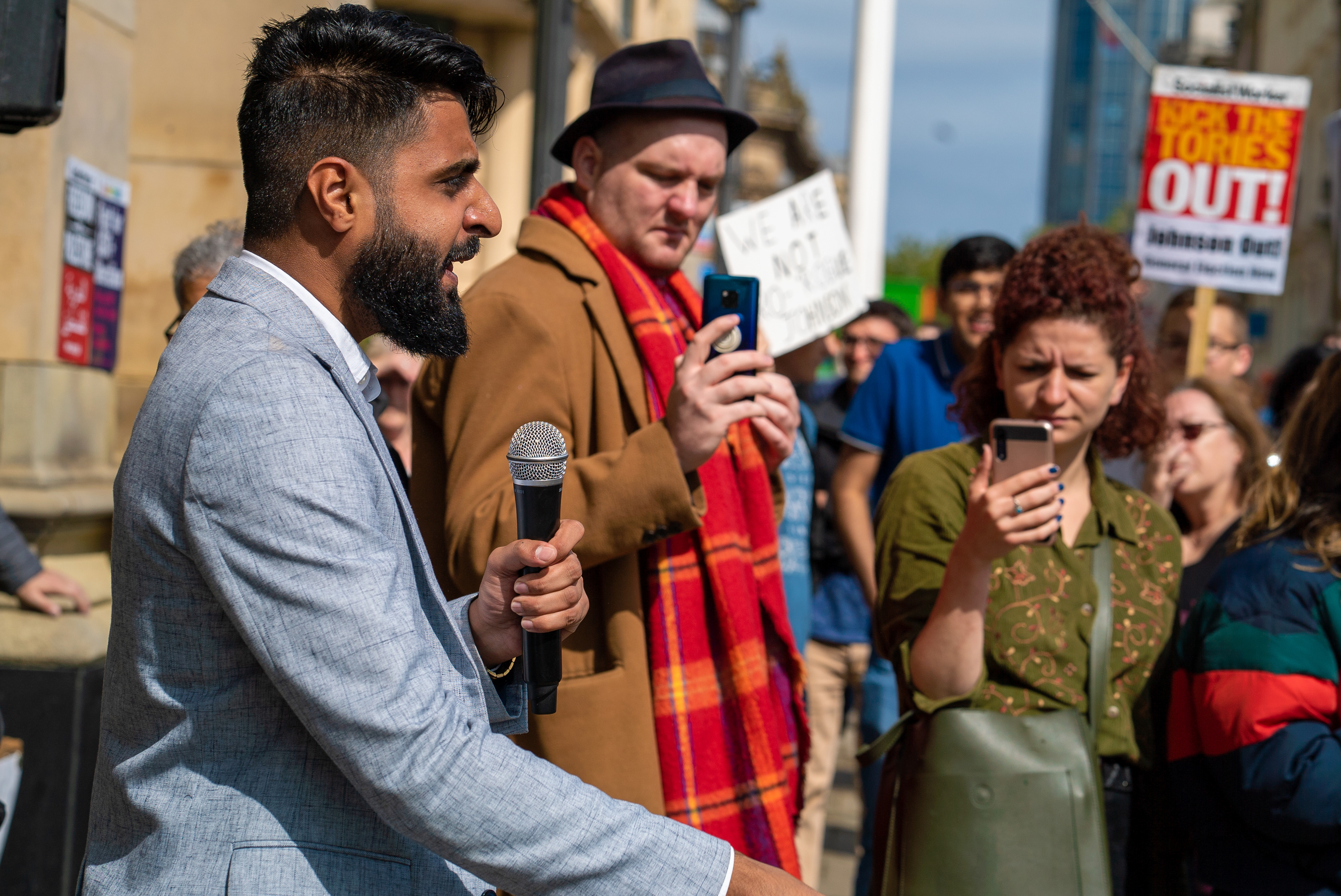 A man holding a microphone whilst making a speech at a protest rally outside of Birmingham Town Hall.