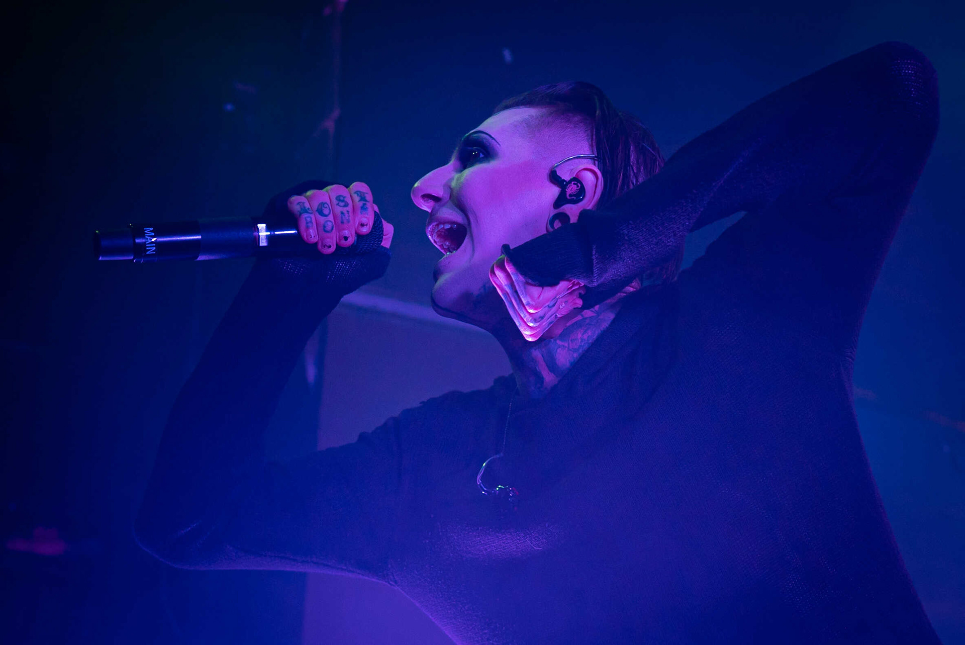 The singer of Motionless in White performing on stage with a microphone in one hand and the other hand in a fist.