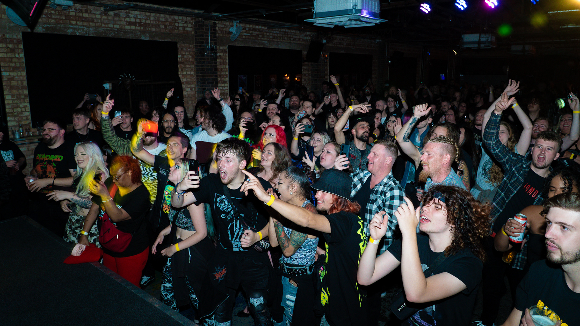 A venue full of people dancing with their arms in the air facing towards the stage.
