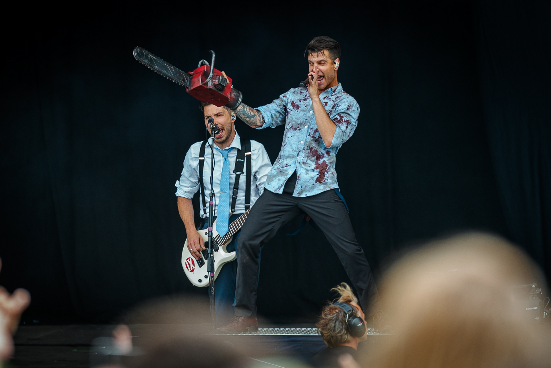 The singer of Ice Nine Kills on stage performing with a microphone in one hand and a chainsaw in another.