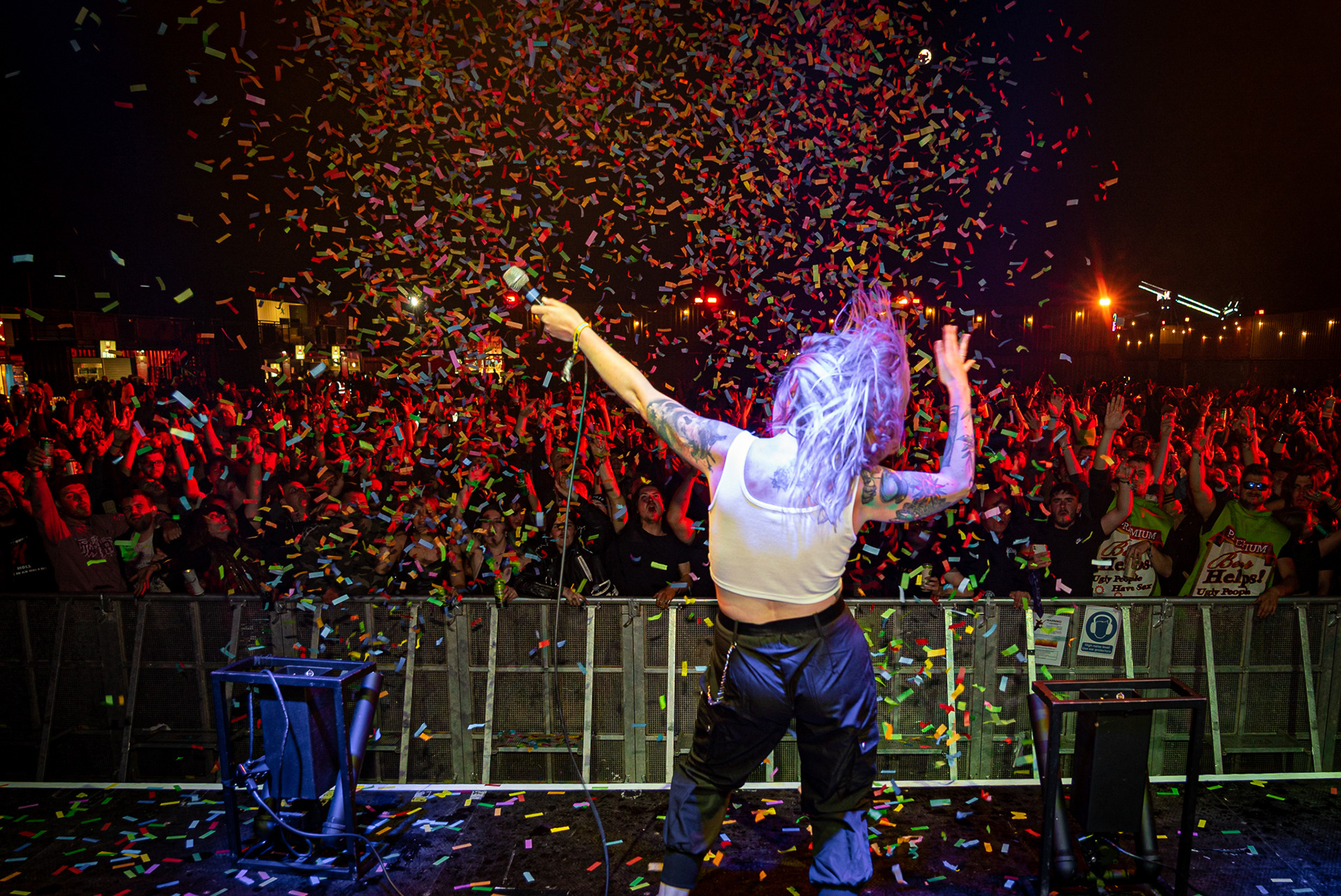 A DJ holding the mic out towards the crowd whilst dancing as confetti canons go off over the huge crowd.