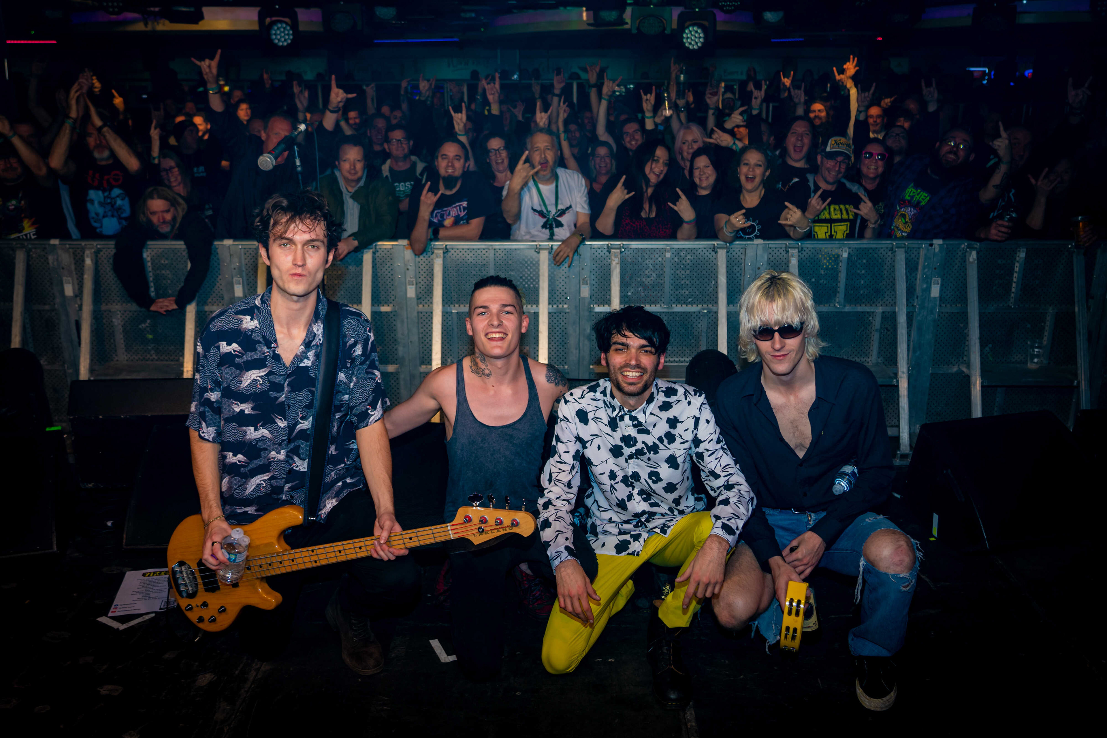 Four members of a band crouched down on stage with their back to the crowd posing for a photo.