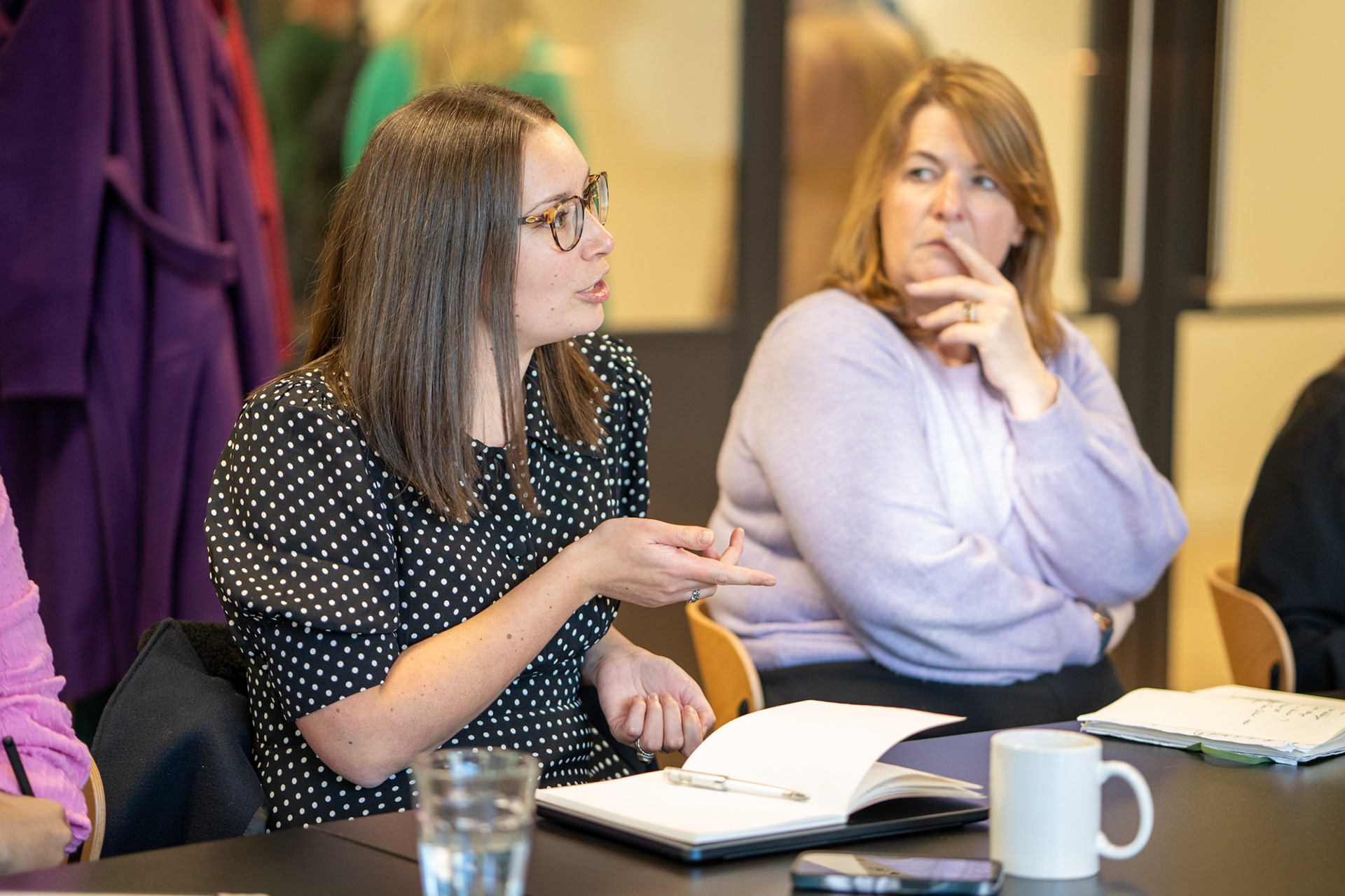 A group of women sitting at a table with books, engaged in a lively discussion and sharing knowledge.