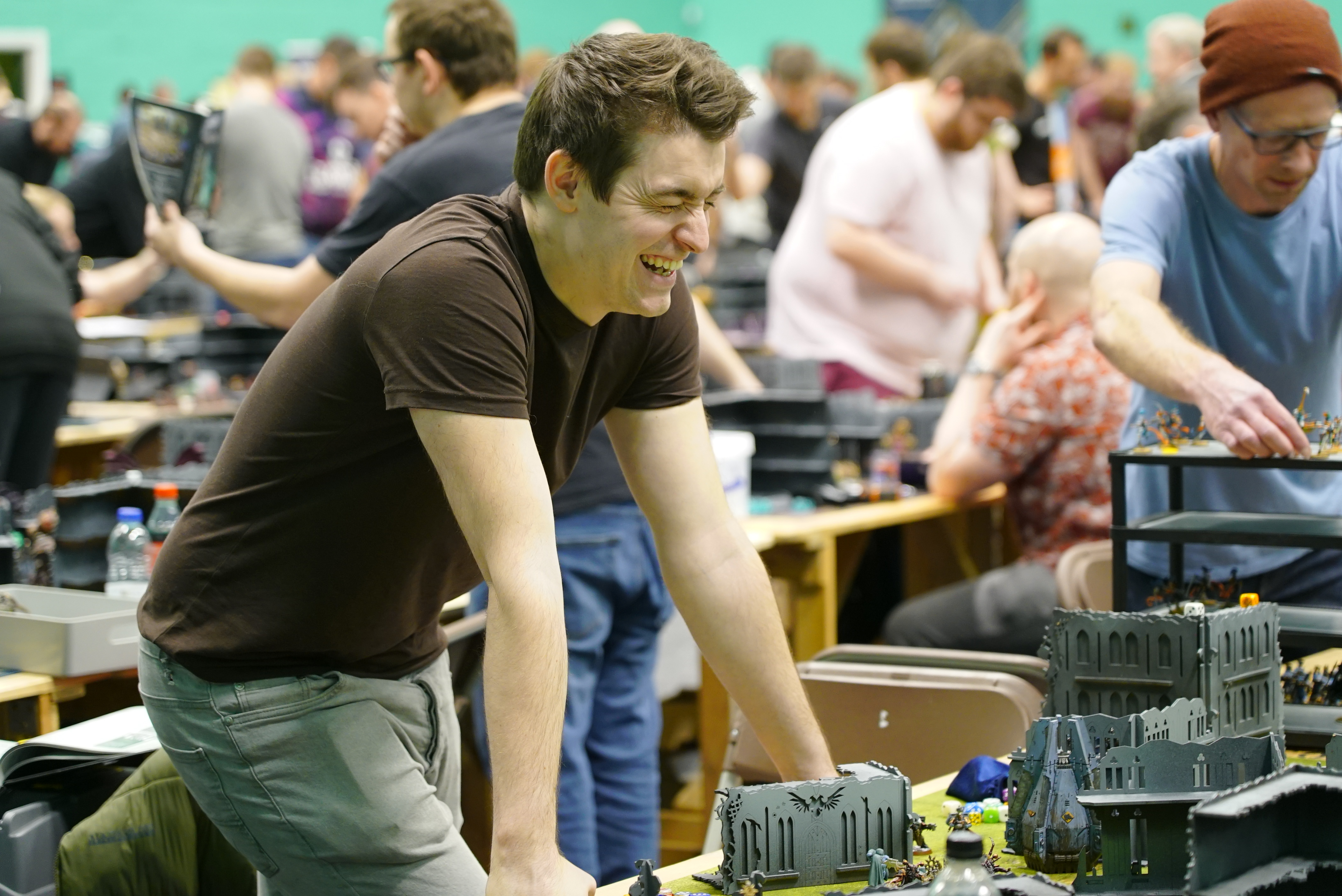  A man leaning on a table laughing as he plays a Warhammer 40k  game during a tournament.