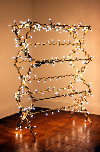 Illumination 1999. Wood, lights. 15” x 30” x 42” Christmas lights are wrapped around a clothes hanger. The soft luminosity glorifies this great household product and reminds the viewer of the warmth of being in a comforting setting / home.