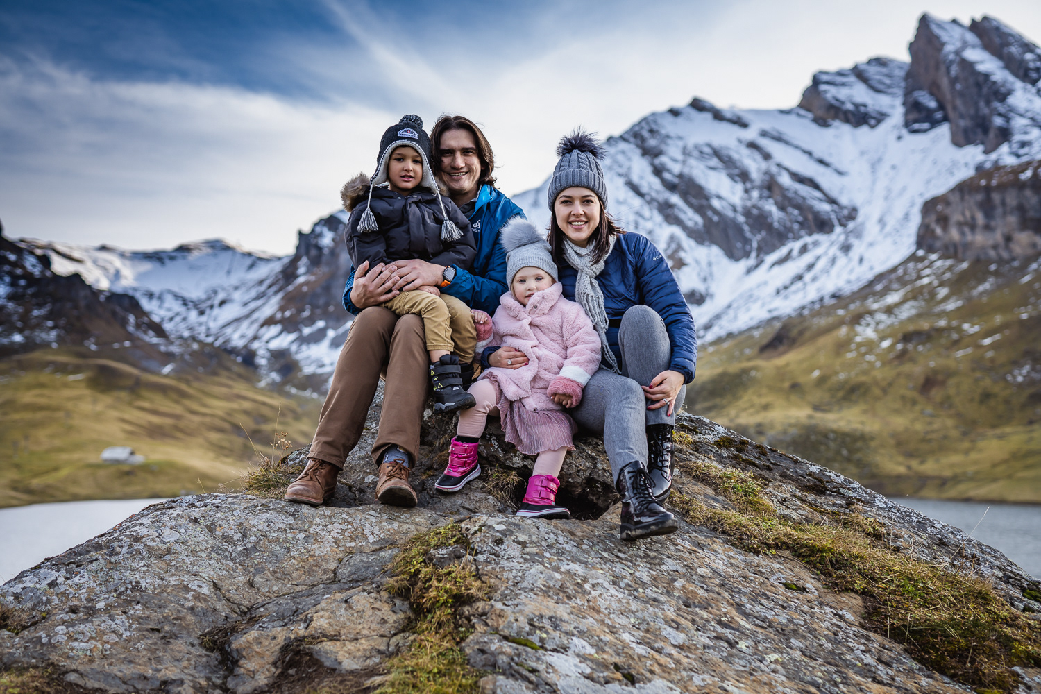 Family of four sitting on the rock during winter photo session in Melchsee Frutt by Adamiak Photography 