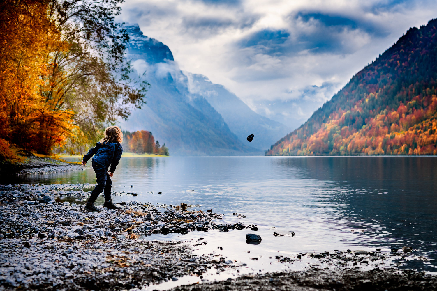 A boy is playing with rocks during his photo session in Klontanersee in Switzerland