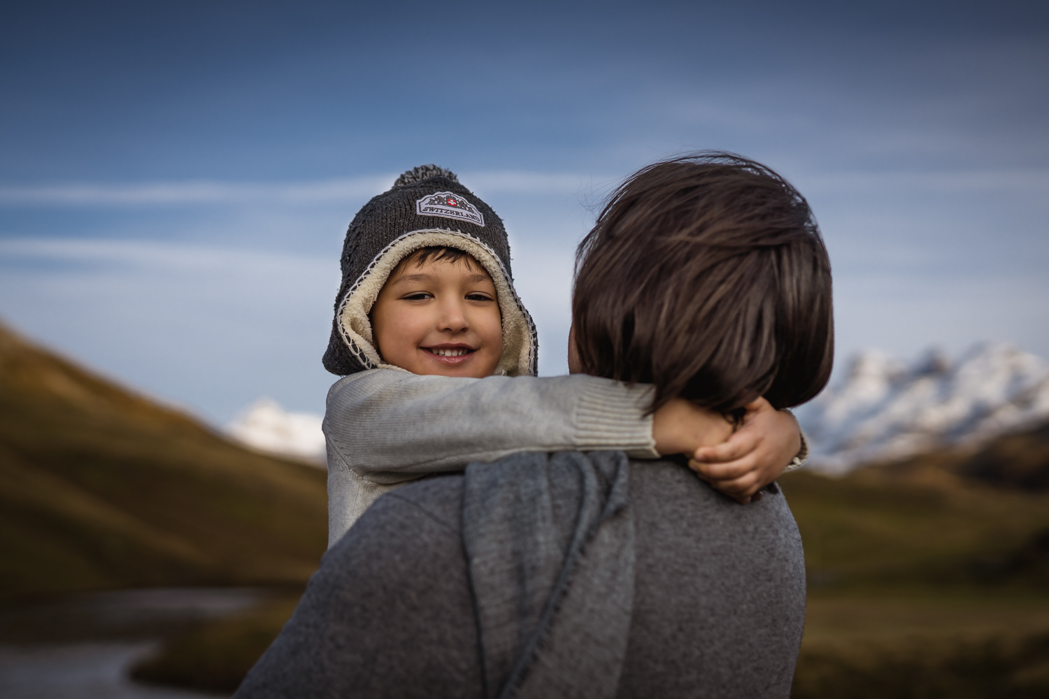 Little boy smiling in father's arms while their family video session in Swiss alps
