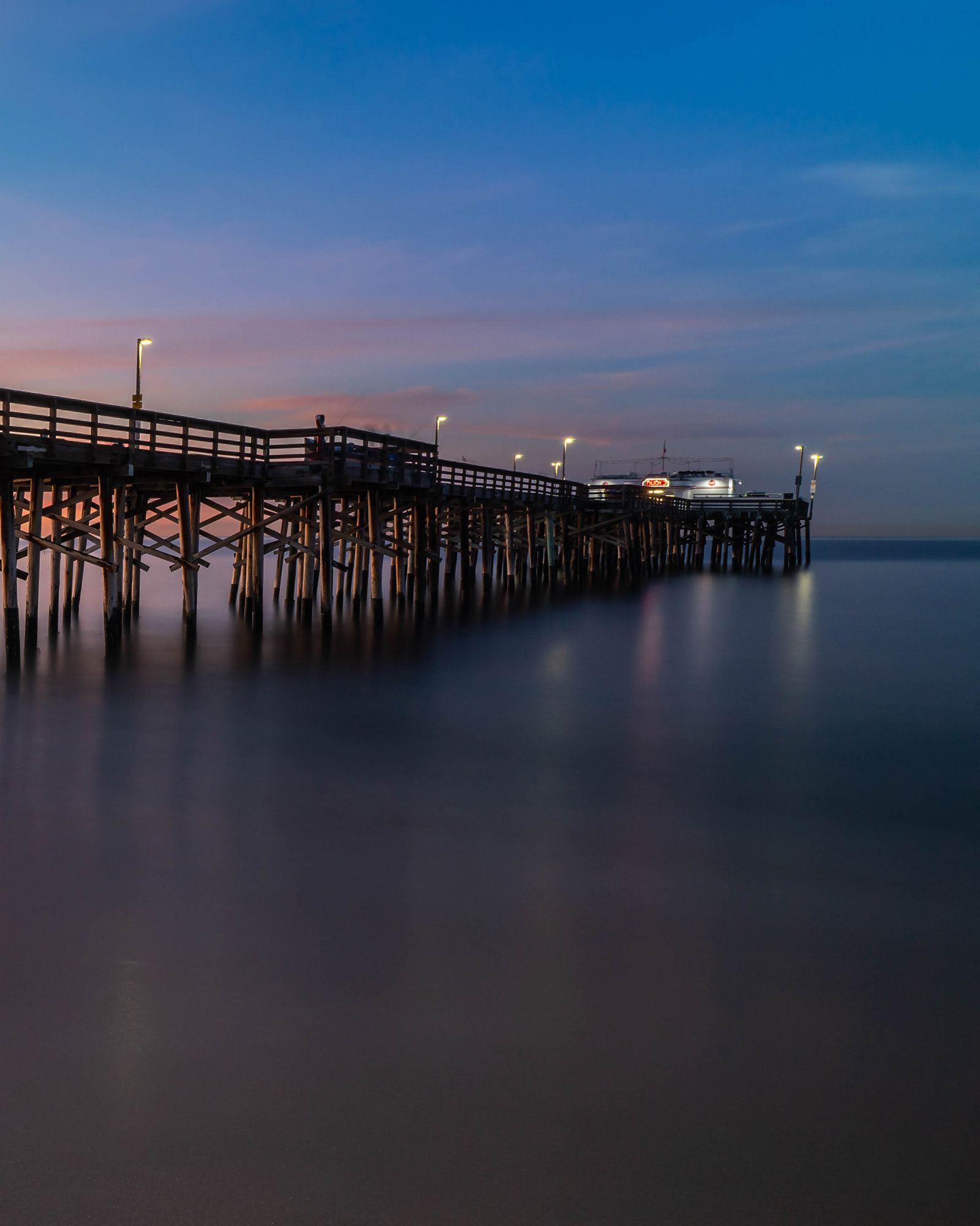 Balboa pier taken as a long exposure before sunup showing the lights of the pier reflecting in the smoothed water