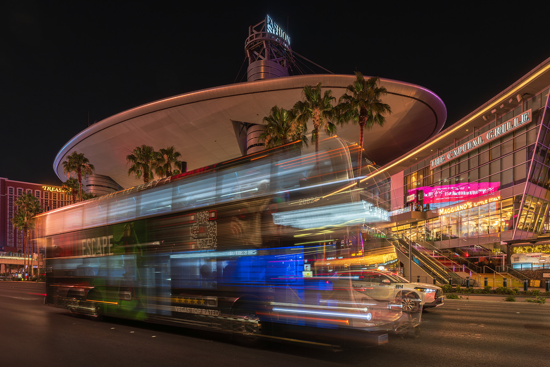 Long exposure of a Deuce double-decker bus shown in motion on the Las Vegas Strip with the Fashion Mall in the background