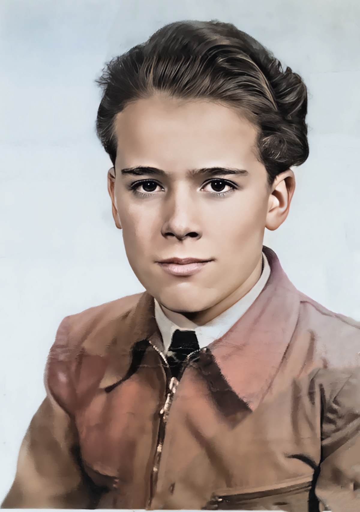 Kolorowany portret młodego chłopca z zaczesanymi do tyłu włosami, ubranego w jasną koszulę, krawat i brązową marynarkę, patrzącego prosto w obiektyw; zdjęcie studyjne z jasnym, jednolitym tłem.