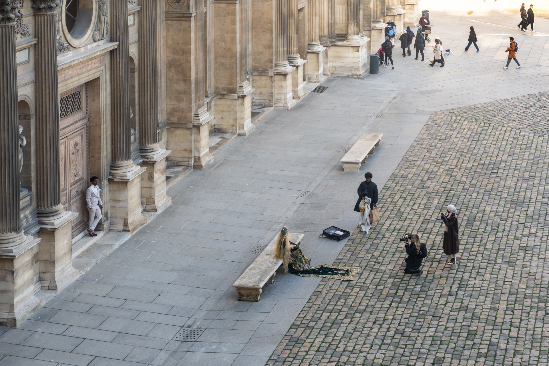 A wedding photographer taking photos of an elaborately dressed bride and groom in the Louvre courtyard.