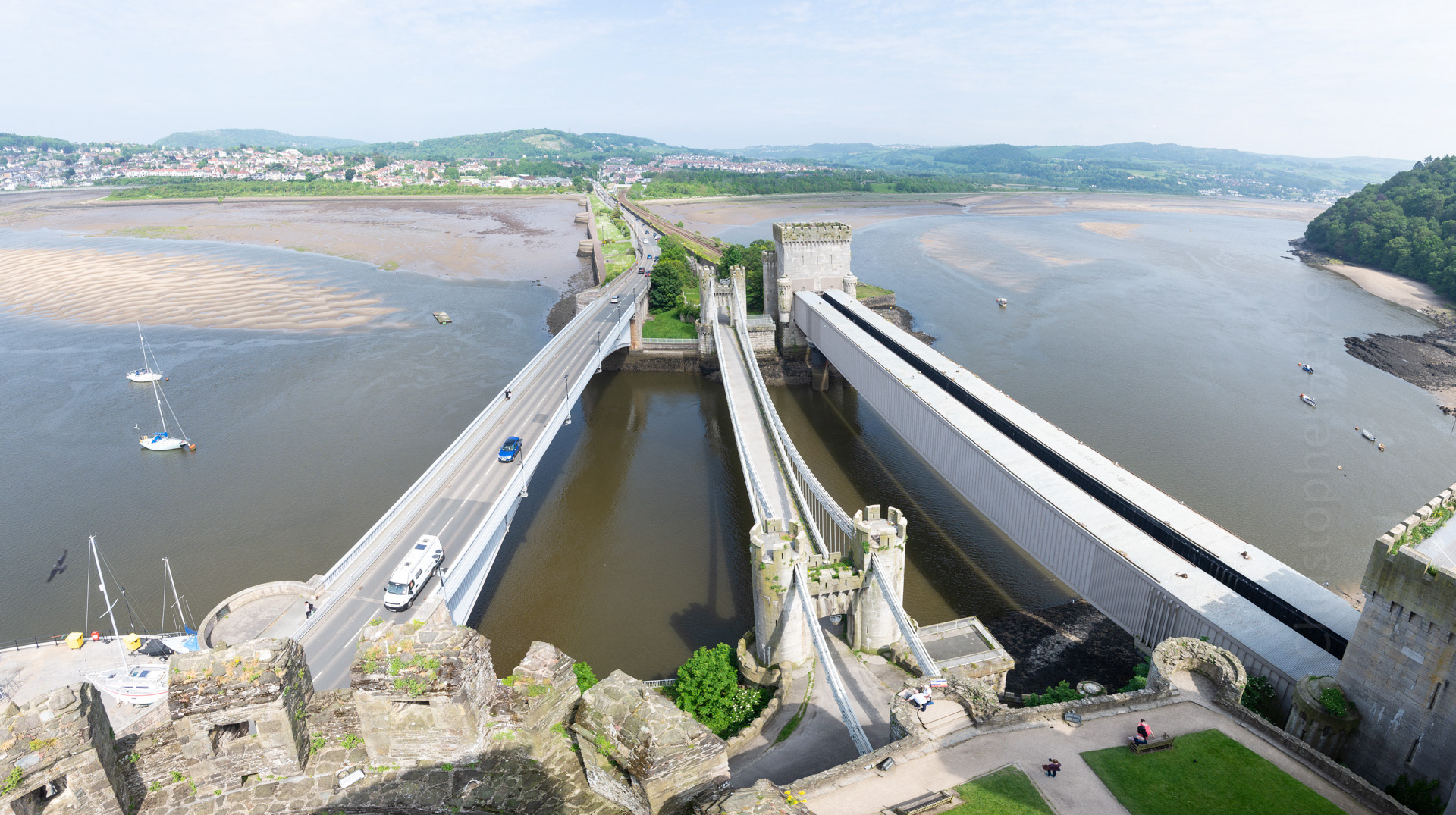 Built from local and imported stone, the castle occupies a coastal ridge, originally overlooking an important crossing over the River Conwy. Today, three bridges and an underground tunnel serve this crossing: an 1826 chain suspension bridge (middle), an 1848 tubular bridge (the first ever! right), a modern 1958 single-arch highway bridge (left), and a 1991 immersed tube (made from a pre-fabricated tube, floated out and sunk to the river bed below.