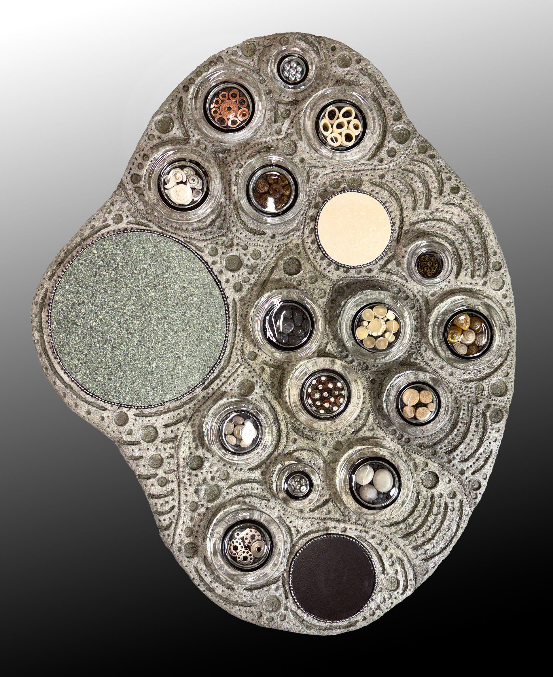 "Round Up"  30"x24"x3"     2026   Glass canister lids, found objects, tumbled creek stones, acorn caps, wood, bone, antler pieces, shells, & porcelain tile set in carved, stained concrete over wediboard.   