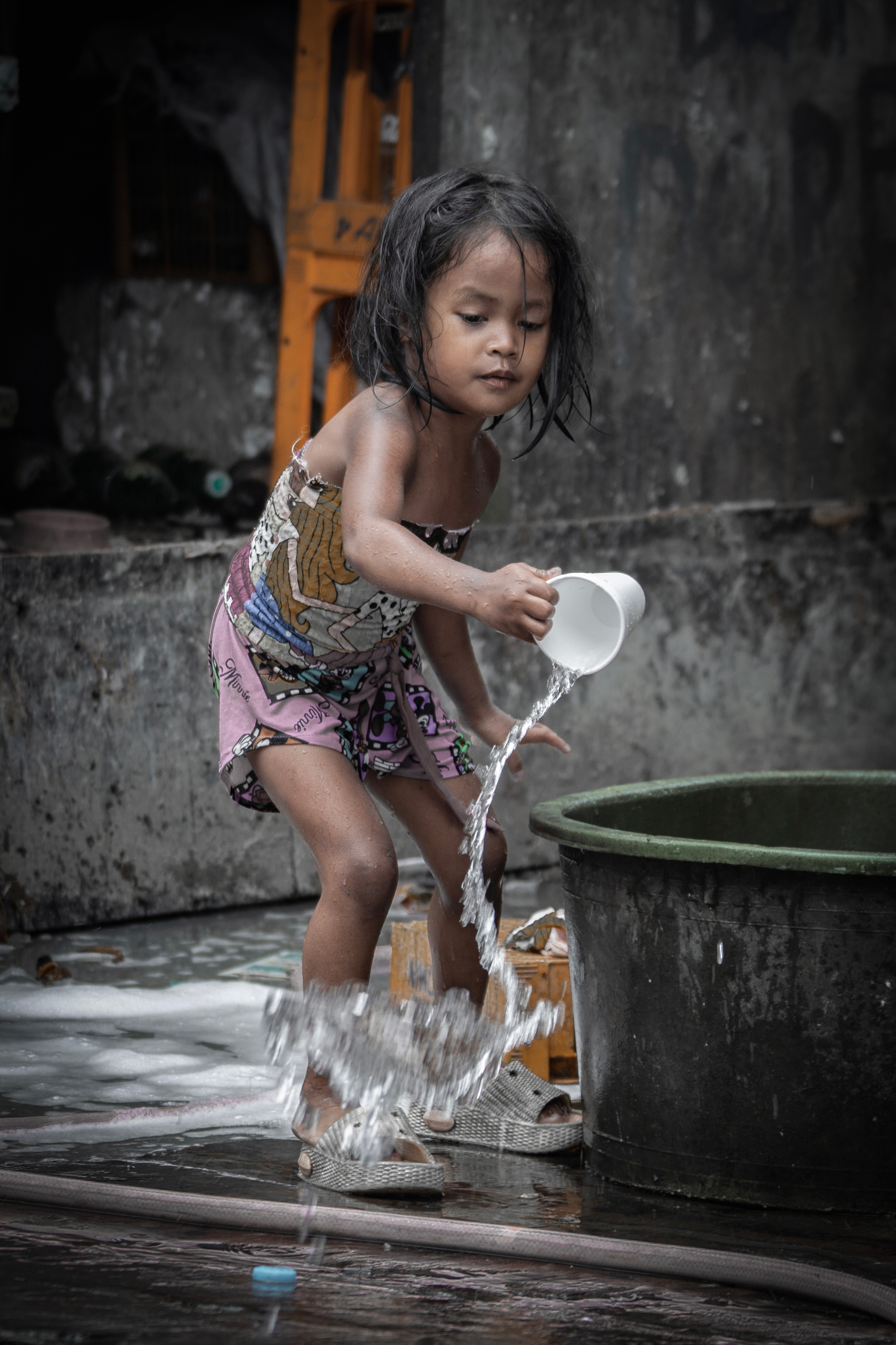 水遊びをする子ども。 遊び道具は井戸水と紙コップのみ。