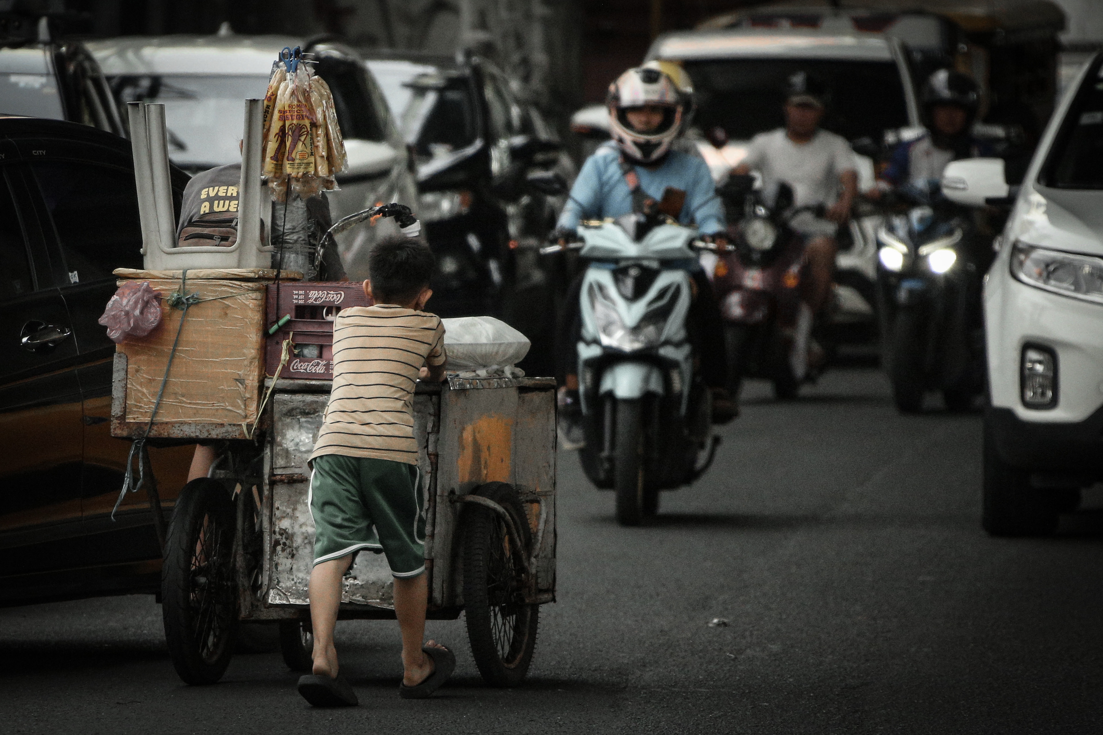 車線を逆走して父親が乗る行商の3輪自転車を押す子ども。数分前に飲み水を与えられていた。