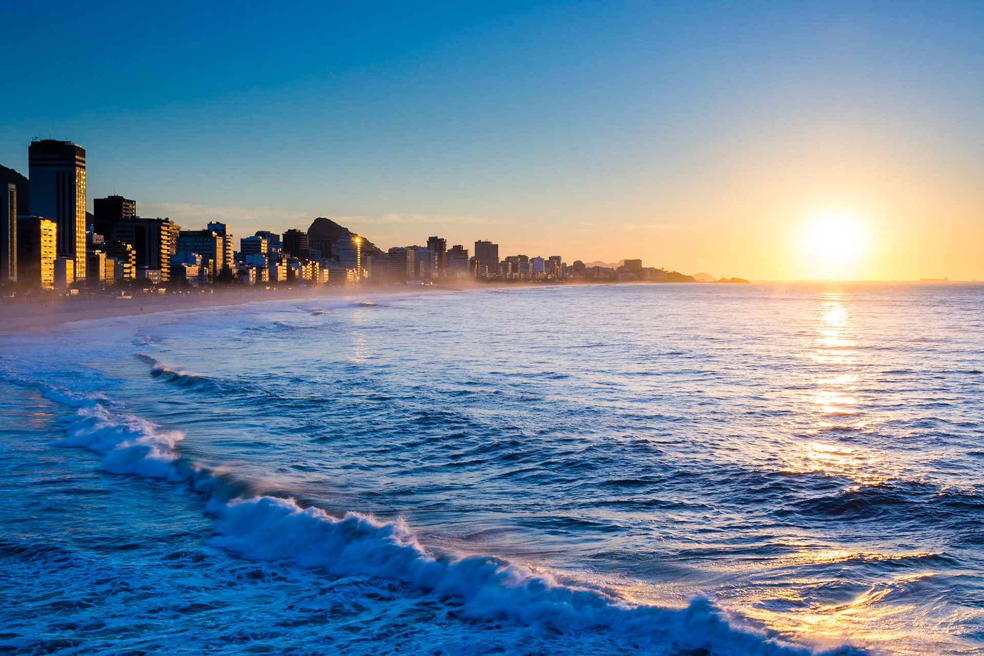 The sun has risen on the breaking waves at Ipanema Beach- the surf is strong enough to create a mist over the beach.