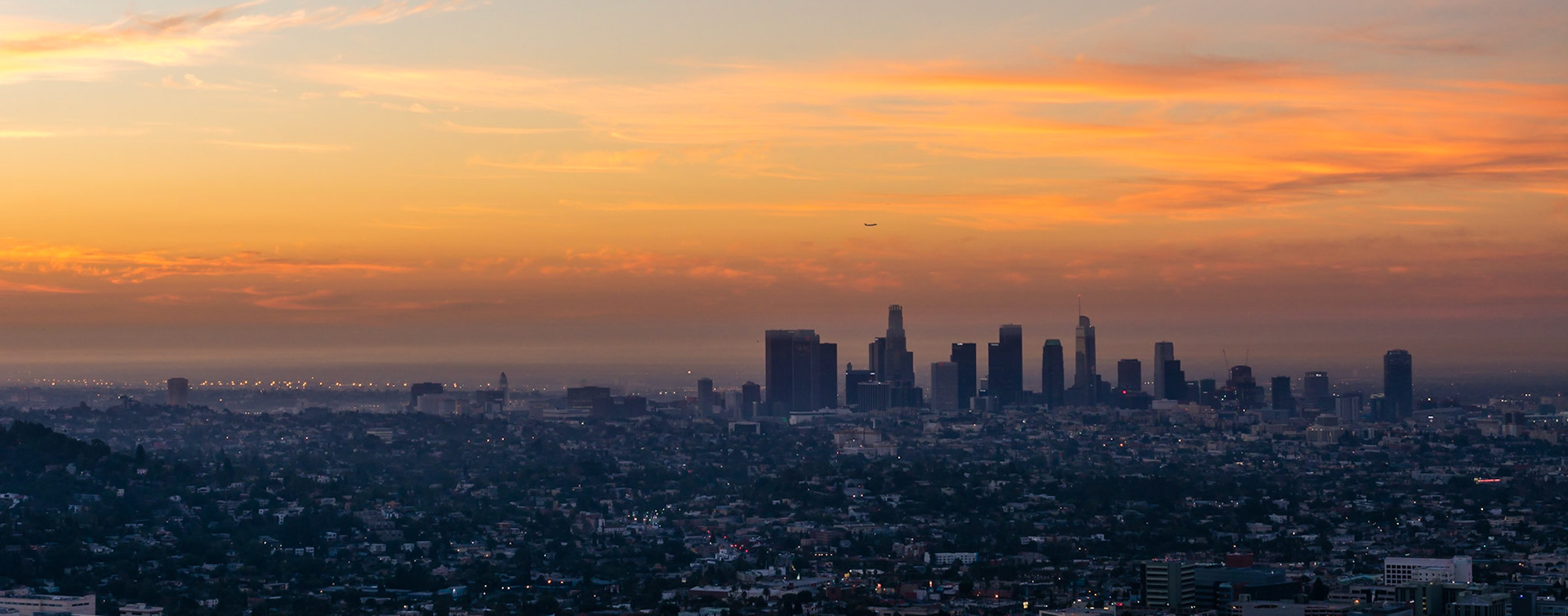 A plane is departing Los Angeles, flying over downtown, shortly before sunrise.
