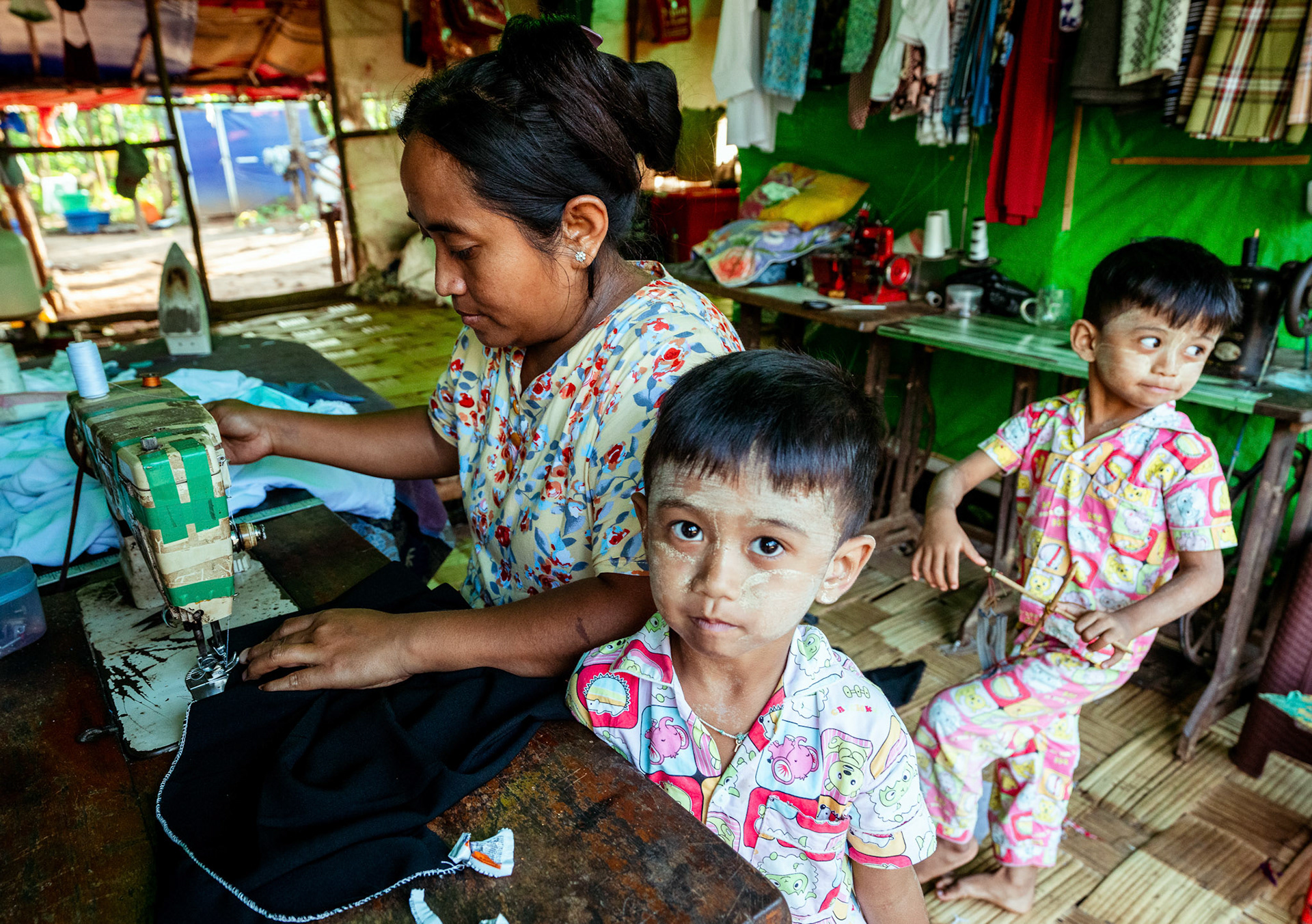 A refugee mother with her twins in Moreh, Manipur, stitching clothes at her home; it comes under the livelihood incubation initiative organised by CRS as a part of COVID-19 Response and Recovery Program.