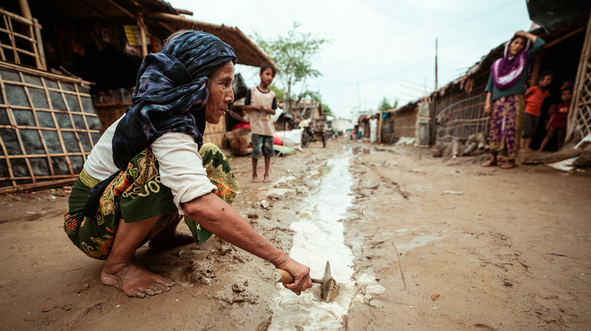A Rohingya refugee clearing a path for accumulated water outside her home during the COVID-19 Response and Recovery Program in Mewat, Haryana
