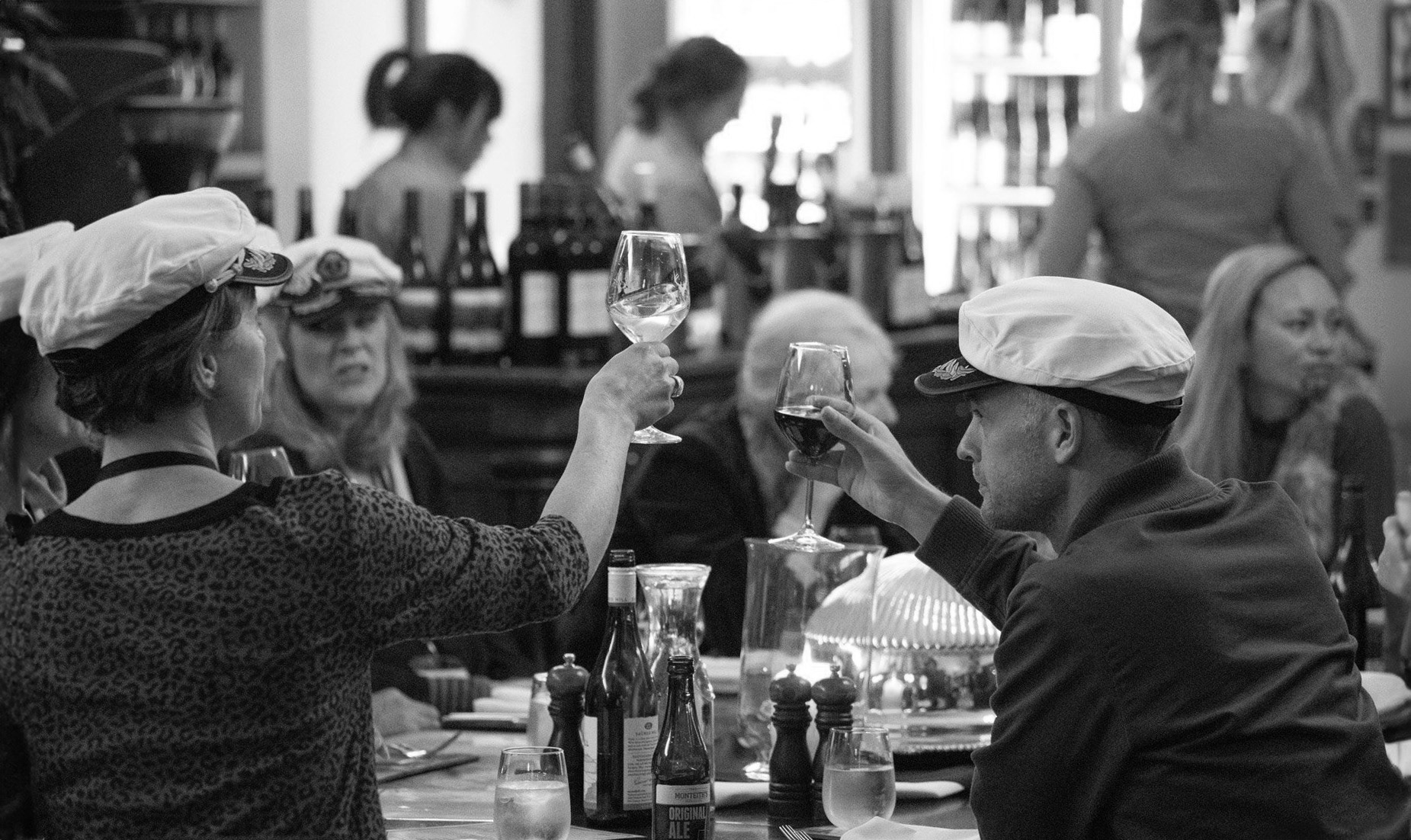 People sat around a table cheers with wine glasses, a bar and staff are in the background