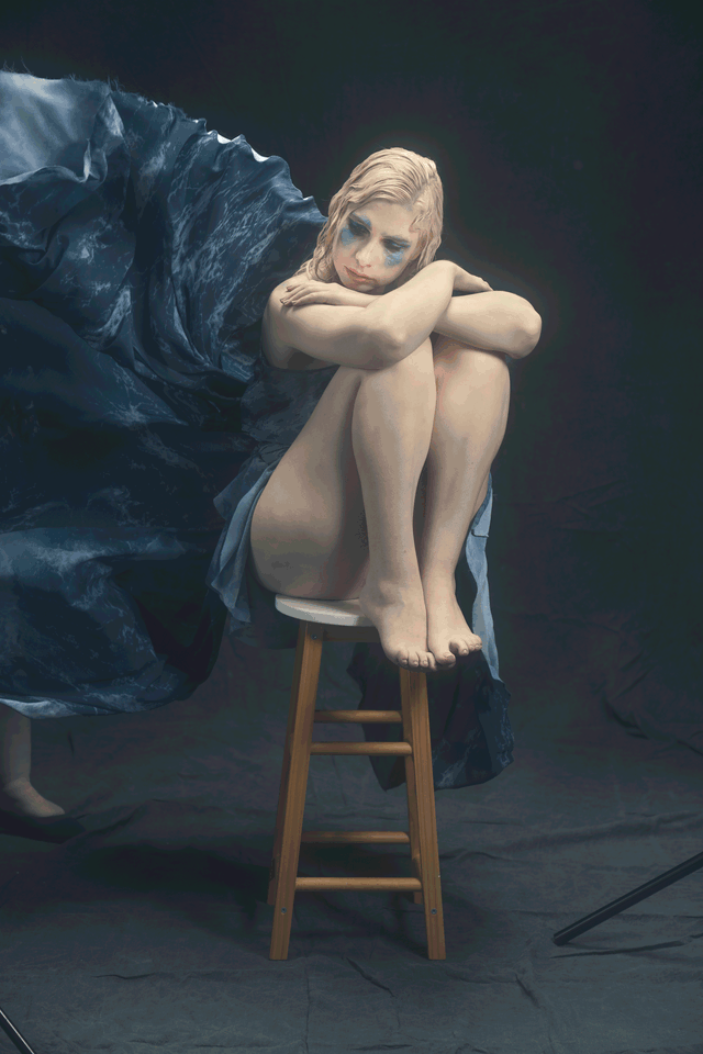 GIF showing time lapse photos of a young woman sat on a stool whilst material that looks like waves is thrown around her