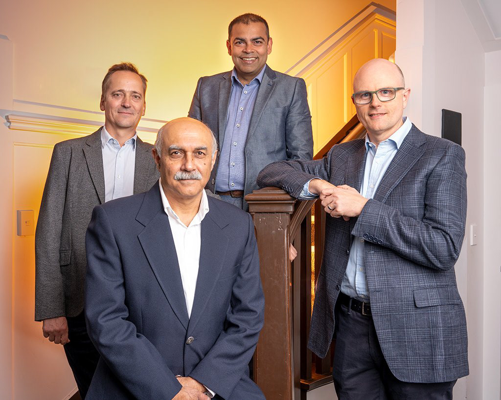Corporate photograph using creative studio lighting showing 4 businessmen in suits, smiling and looking smart and confident