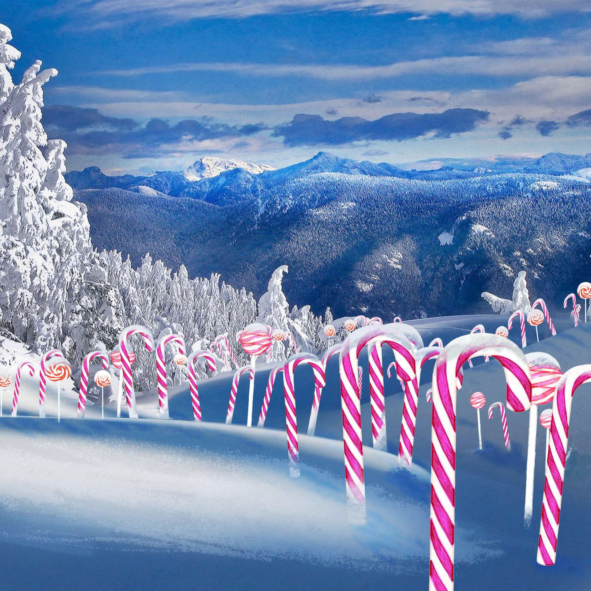 A winter scene with blue skies, mountains, and snow covered trees. There are pink and white candy canes  and lollipops topped with snow throughout the hills in the front. A 