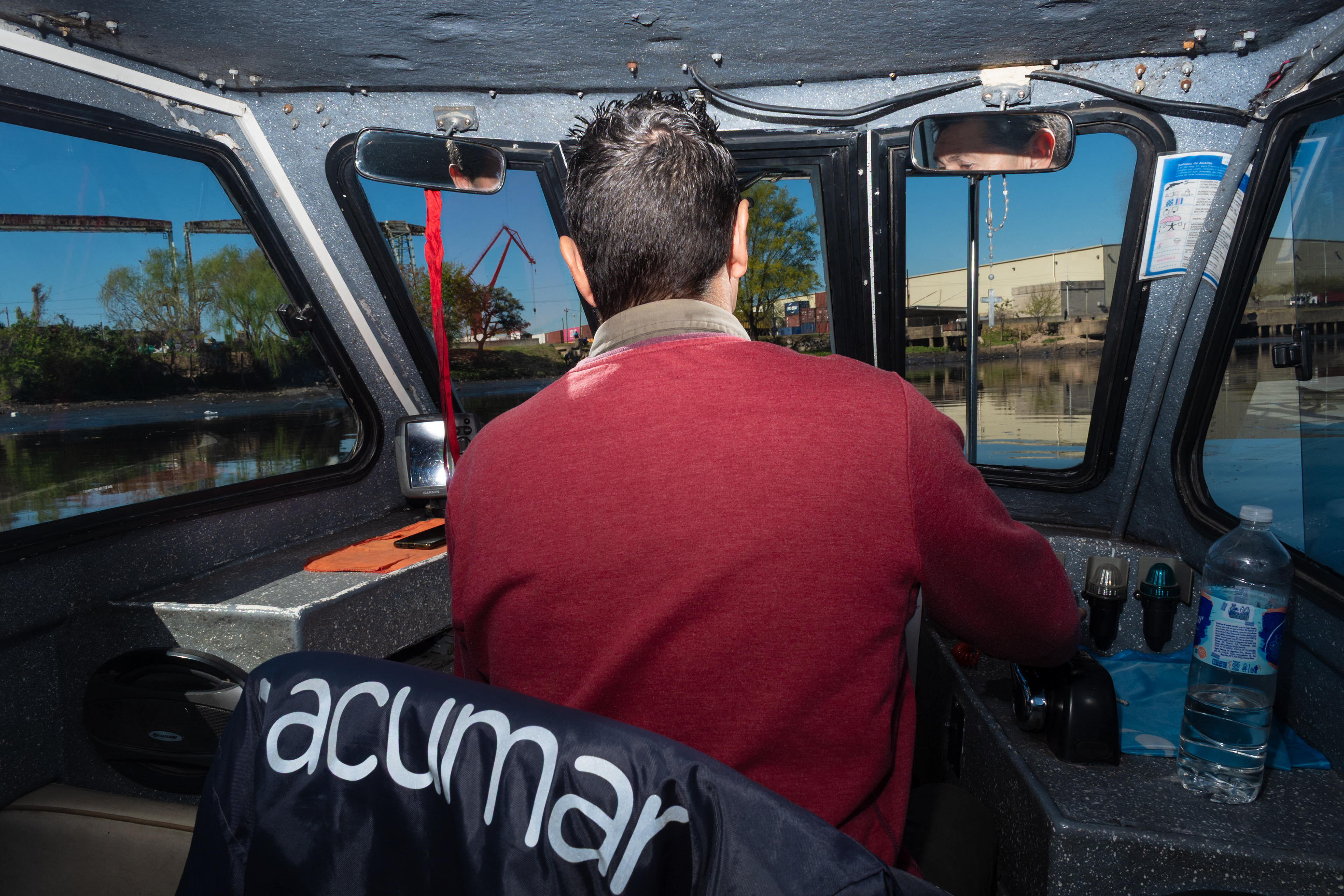 An ACUMAR boat pilot navigates his vessel collecting floating refuse and cleaning the polluted Riachuelo River during a routine control operation.