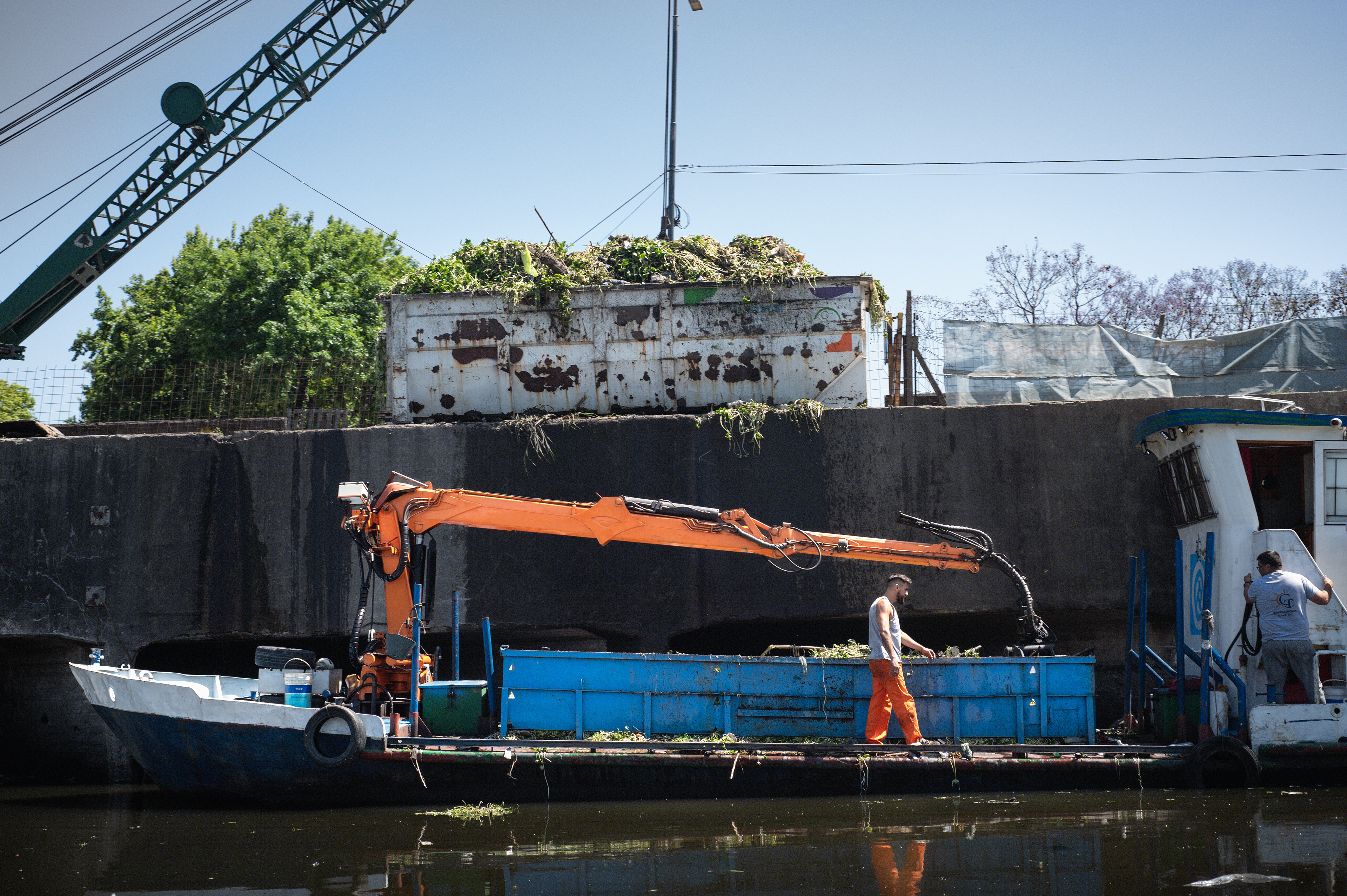 Sanitation workers from ACUMAR operate a crane boat with which they remove waste from the surface of the Riachuelo river, during the daily cleanup up.