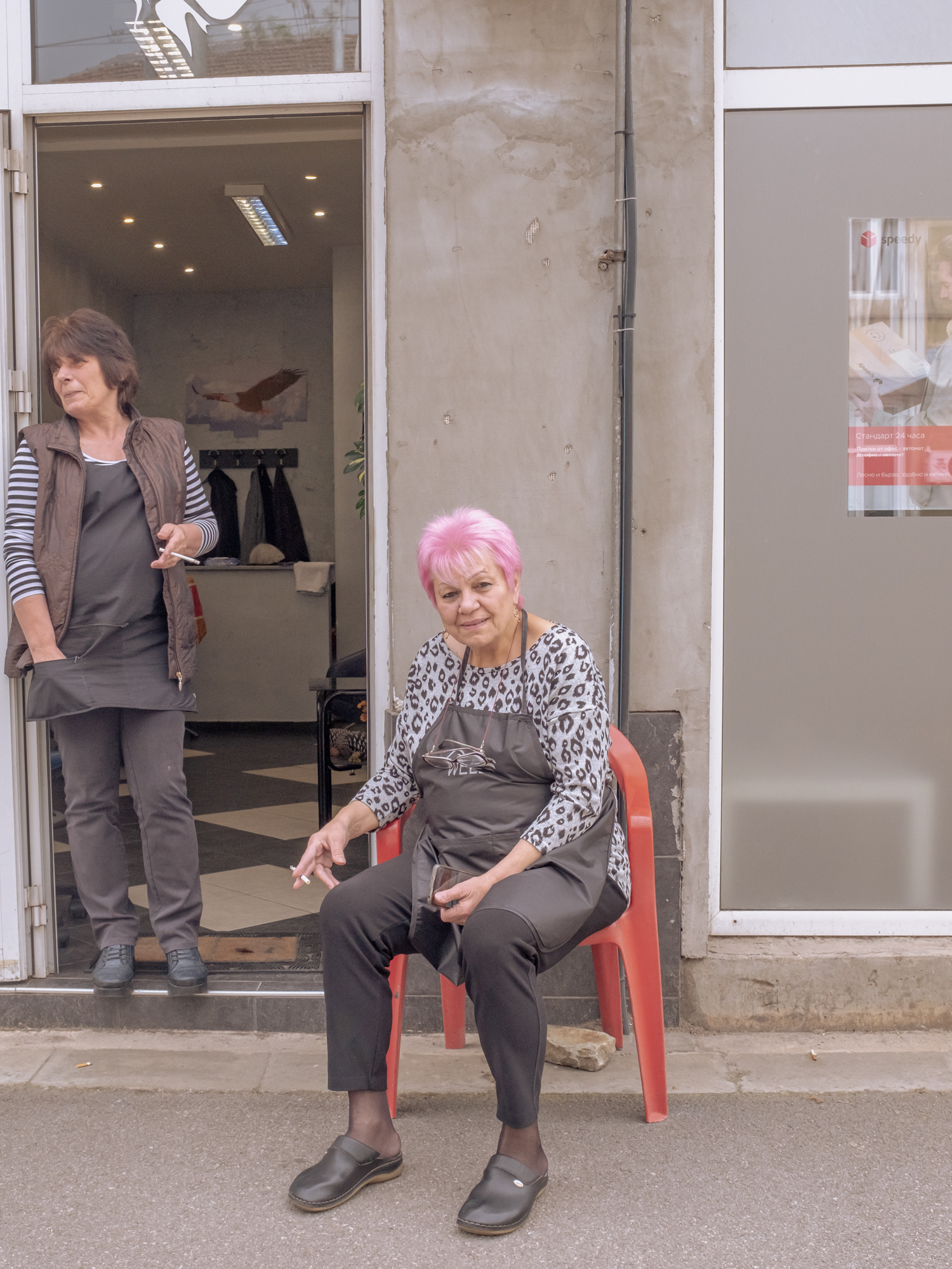 old lady smoking in front of a hairdressera boy fighting with a stick, Sofia Bulgaria 2024